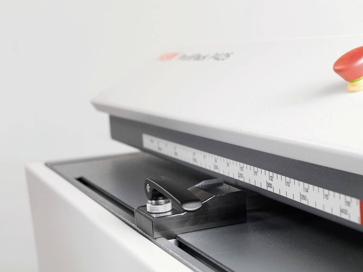 Papier-Schneidemaschine mit Messskala und rotem Sicherheitsknopf auf der Oberseite. Eignet sich für präzise Papierschnitte in Büro oder Druckerei.