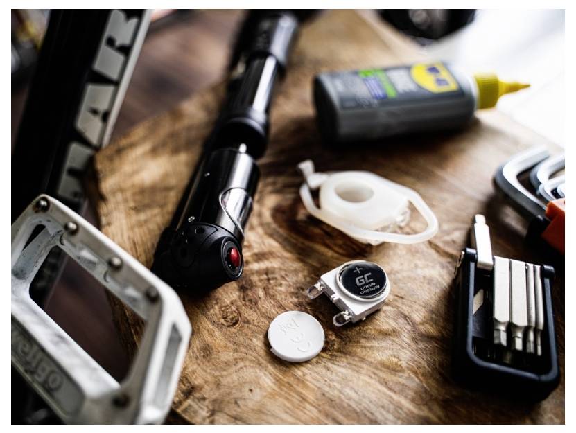 Reparaturwerkzeuge und Zubehör auf einem Holzbrett, darunter eine Pumpe, Schmieröl, Klebeband, ein Inbusschlüssel-Set und Knopfzellen.