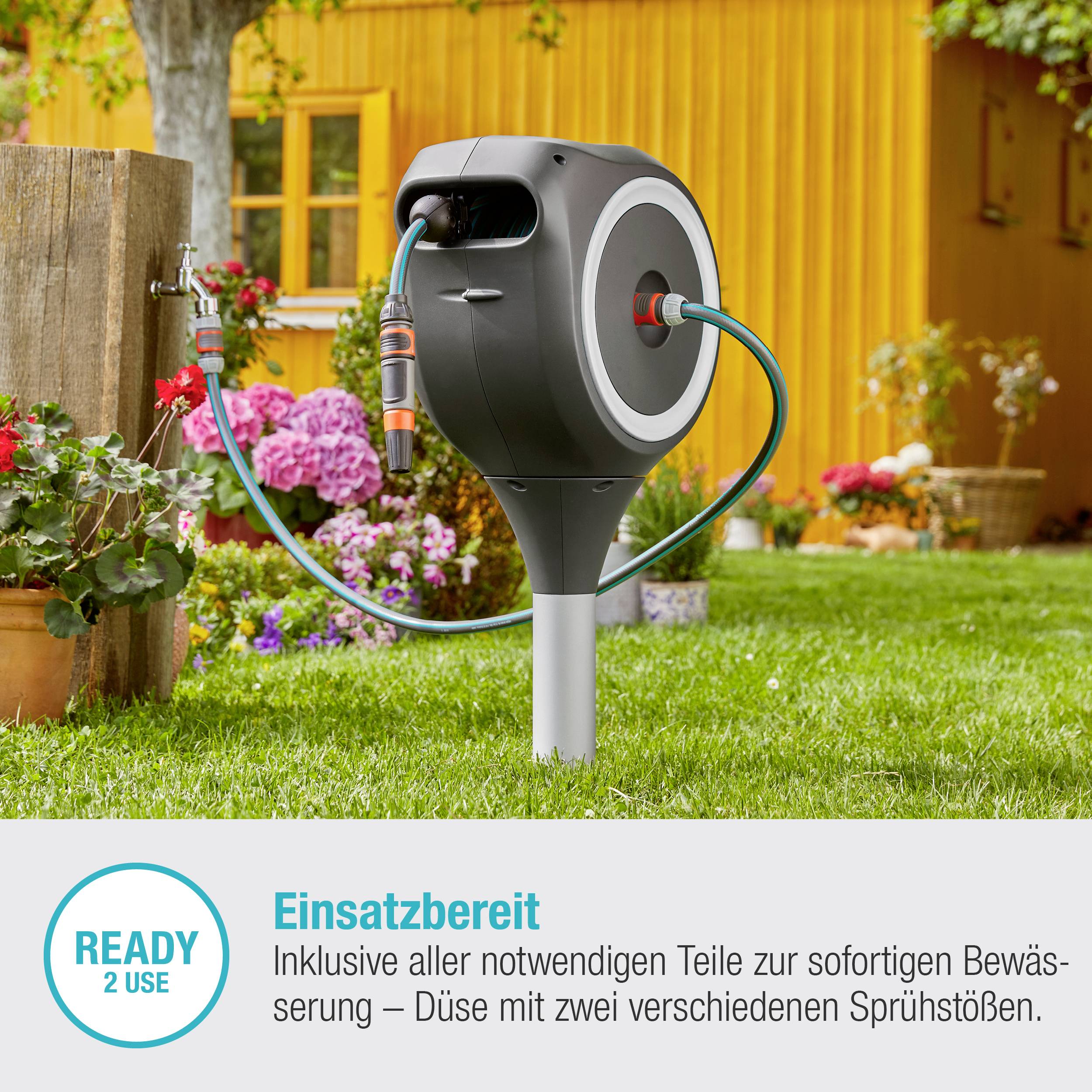 Gartenschlauchaufroller im Blumengarten. Bereit zur Bewässerung mit variabler Sprühdüse. Text: 'Einsatzbereit - READY 2 USE'.