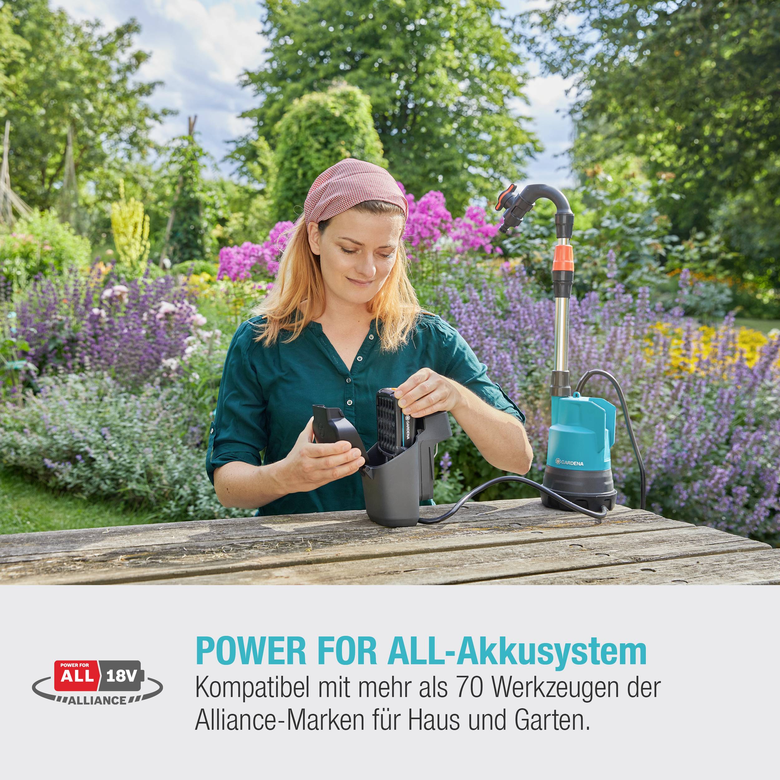 Eine Person lädt eine Batterie mit einem Akkuladegerät im Freien auf. Im Hintergrund sind farbenfrohe Blumen zu sehen. Text: 'Power for All-Akkusystem'.