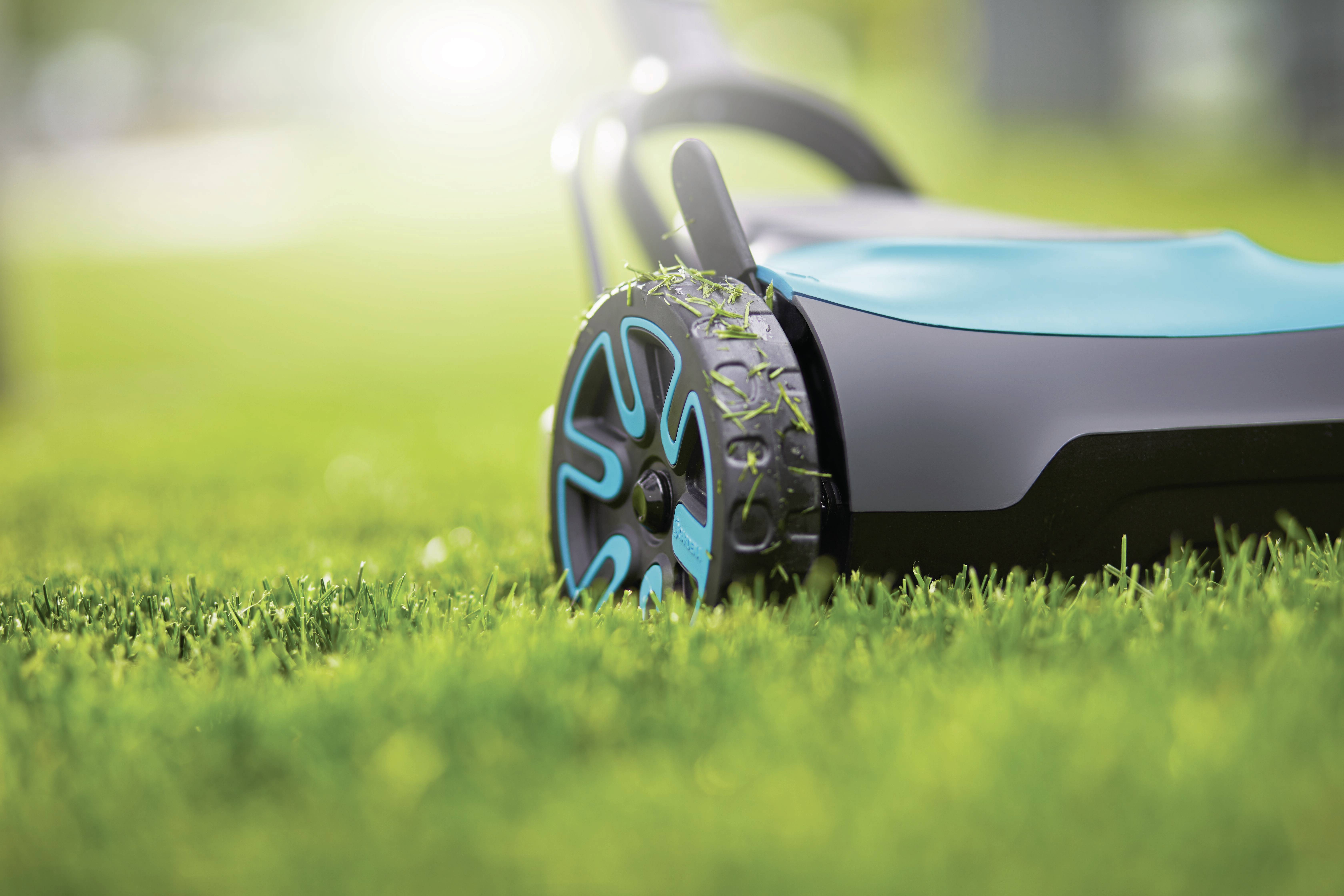 Ein moderner Rasenmäher mäht frisches, grünes Gras bei sonnigem Wetter. Der Fokus liegt auf dem Rad, das Grasreste aufweist.