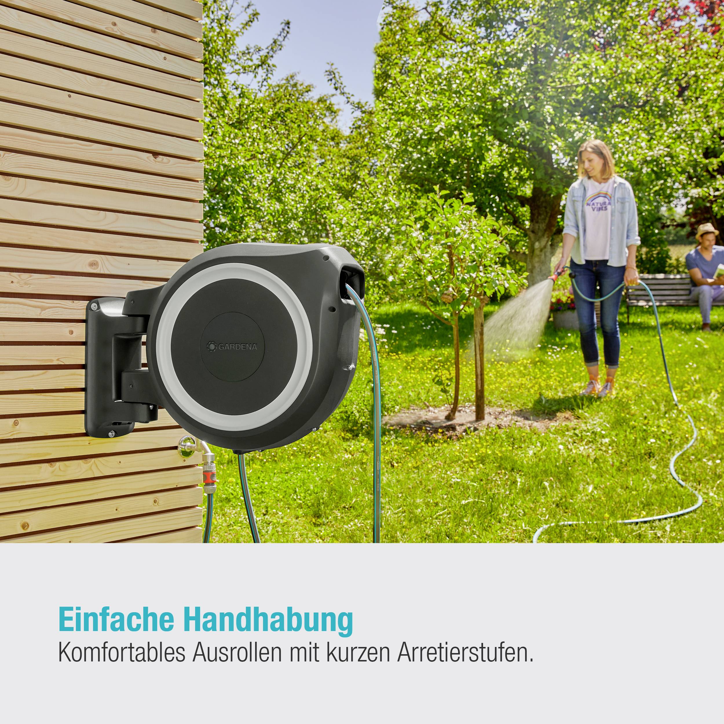 Eine Frau im Garten rollt einen grünen Wasserschlauch von einer Wandhalterung ab. Im Hintergrund Bäume und Sträucher. Text: 'Einfache Handhabung'.