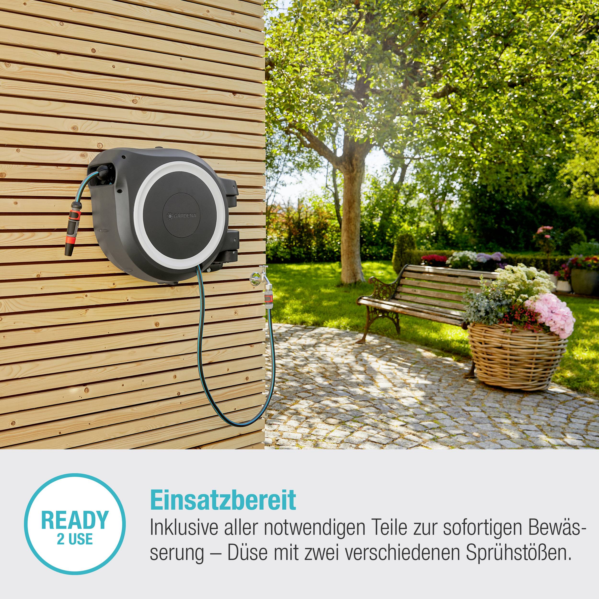 Eine automatische Gartenschlauchrolle ist an einer Holzwand montiert. Auf der linken Seite steht: 'Einsatzbereit - Inklusive aller notwendigen Teile zur sofortigen Bewässerung'. Im Hintergrund sind Bäume und ein Pflanzkübel sichtbar.