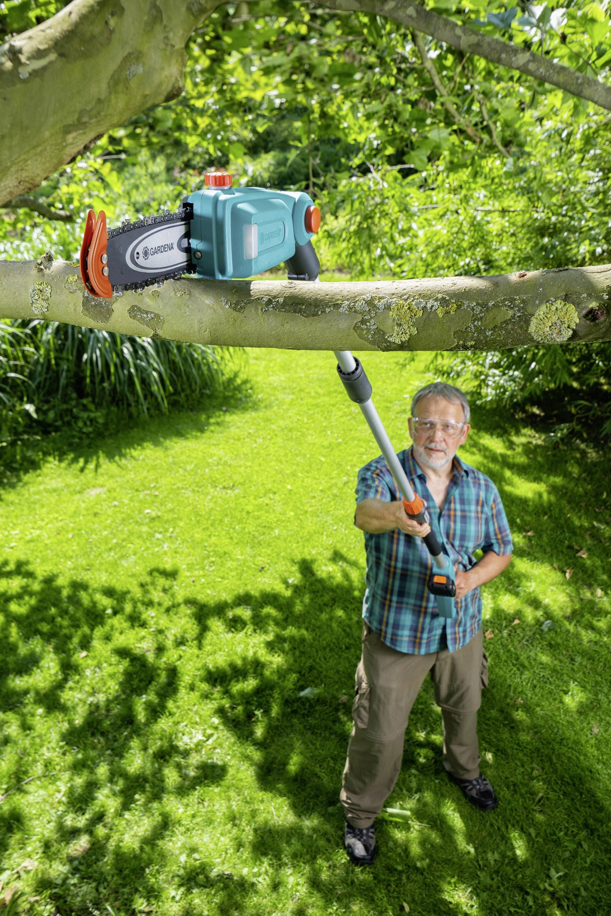 Eine Person verwendet eine Teleskop-Astsäge, um einen Ast von einem Baum in einem grünen Garten zu schneiden.