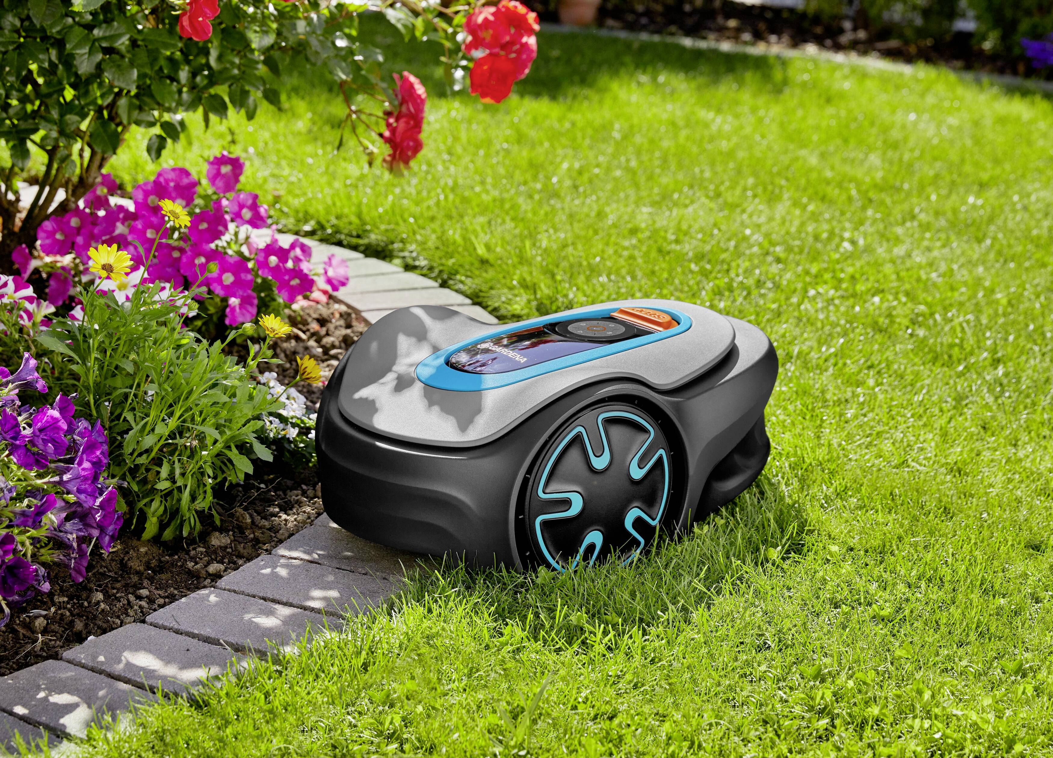 Ein Rasenmäherroboter mäht neben einem Blumenbeet mit bunten Blumen auf grünem Rasen.