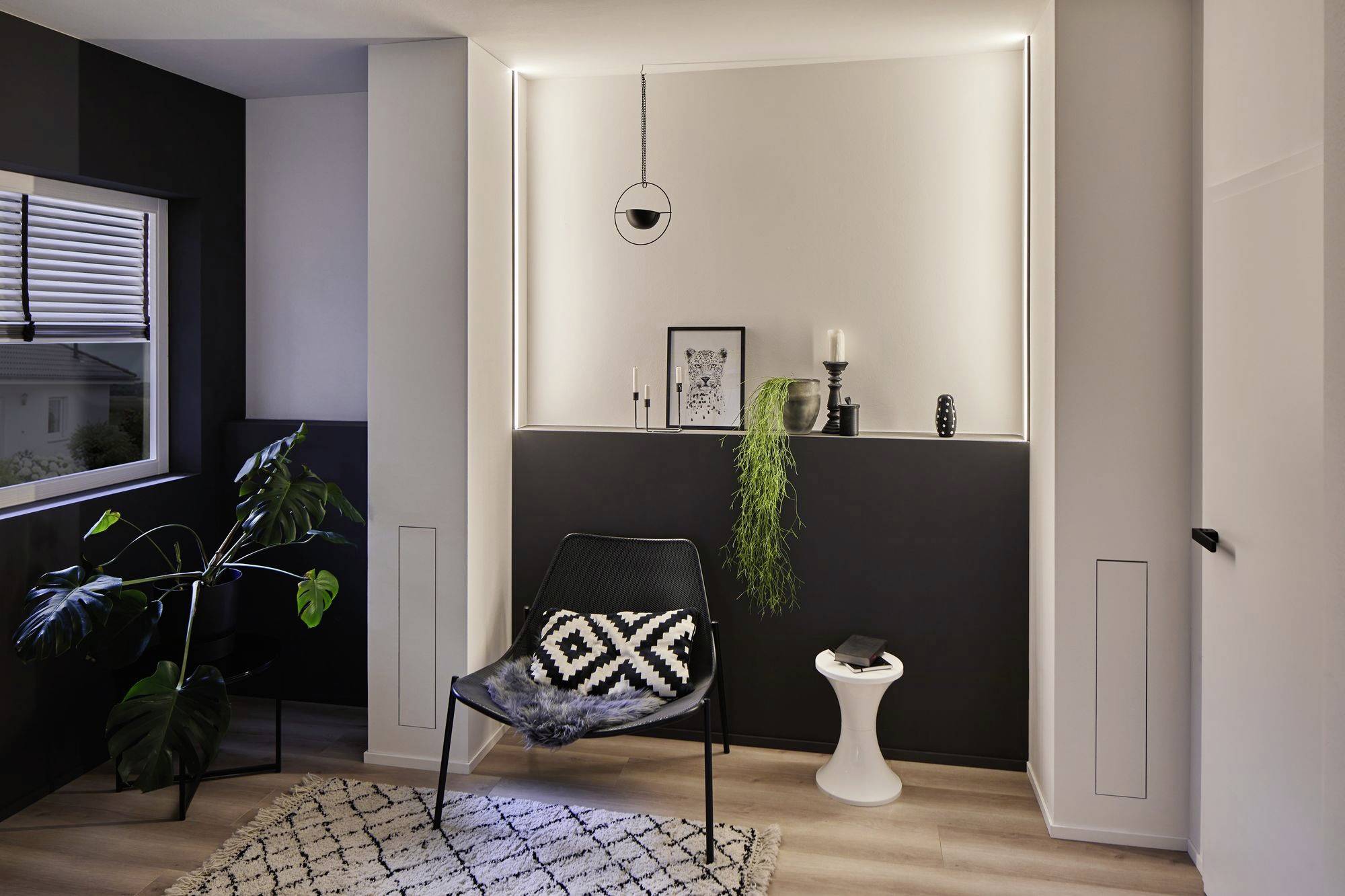 Ein modernes Wohnzimmer mit einem schwarzen Stuhl, Pflanzen und minimalistischer Dekoration. Warme Beleuchtung und helle Holzböden.