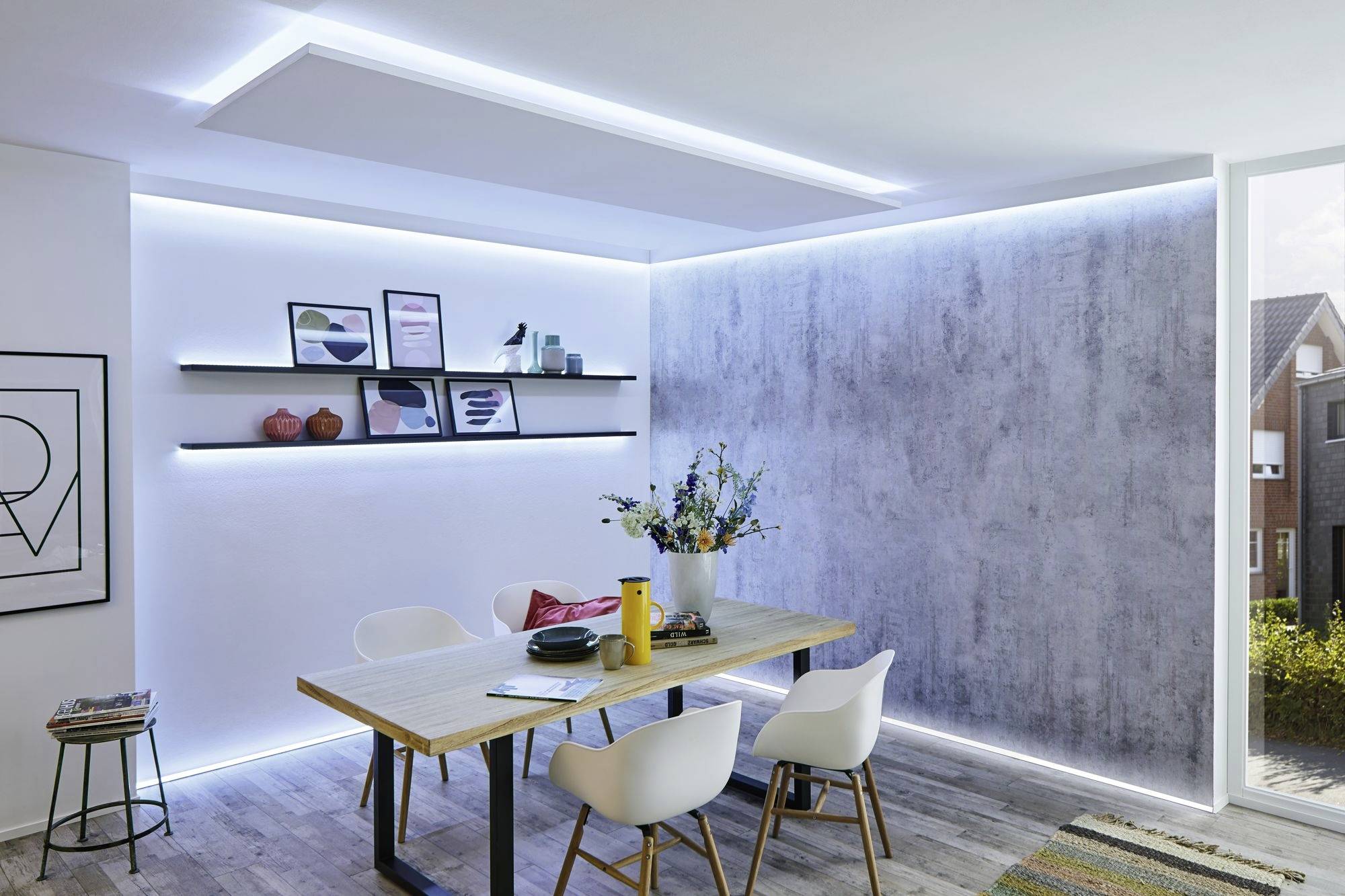 Moderner Essbereich mit Holztisch, weißen Stühlen und dekorativen Regalen an der Wand. Helle LED-Beleuchtung und frische Blumen.