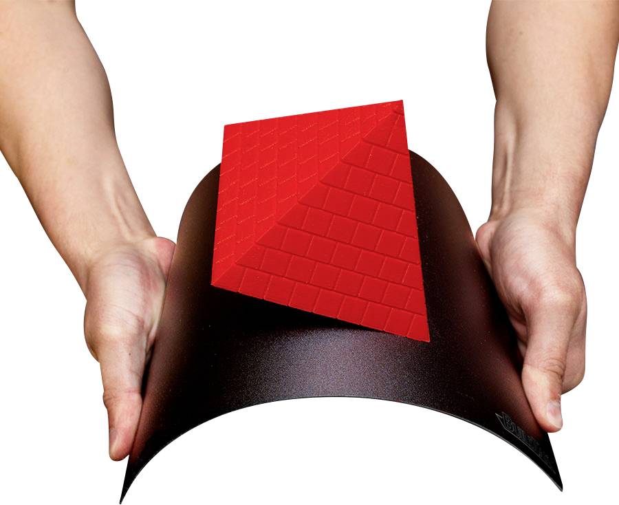 Zwei Hände halten eine geformte schwarze Fläche mit einem roten, viereckigen Körper darauf.