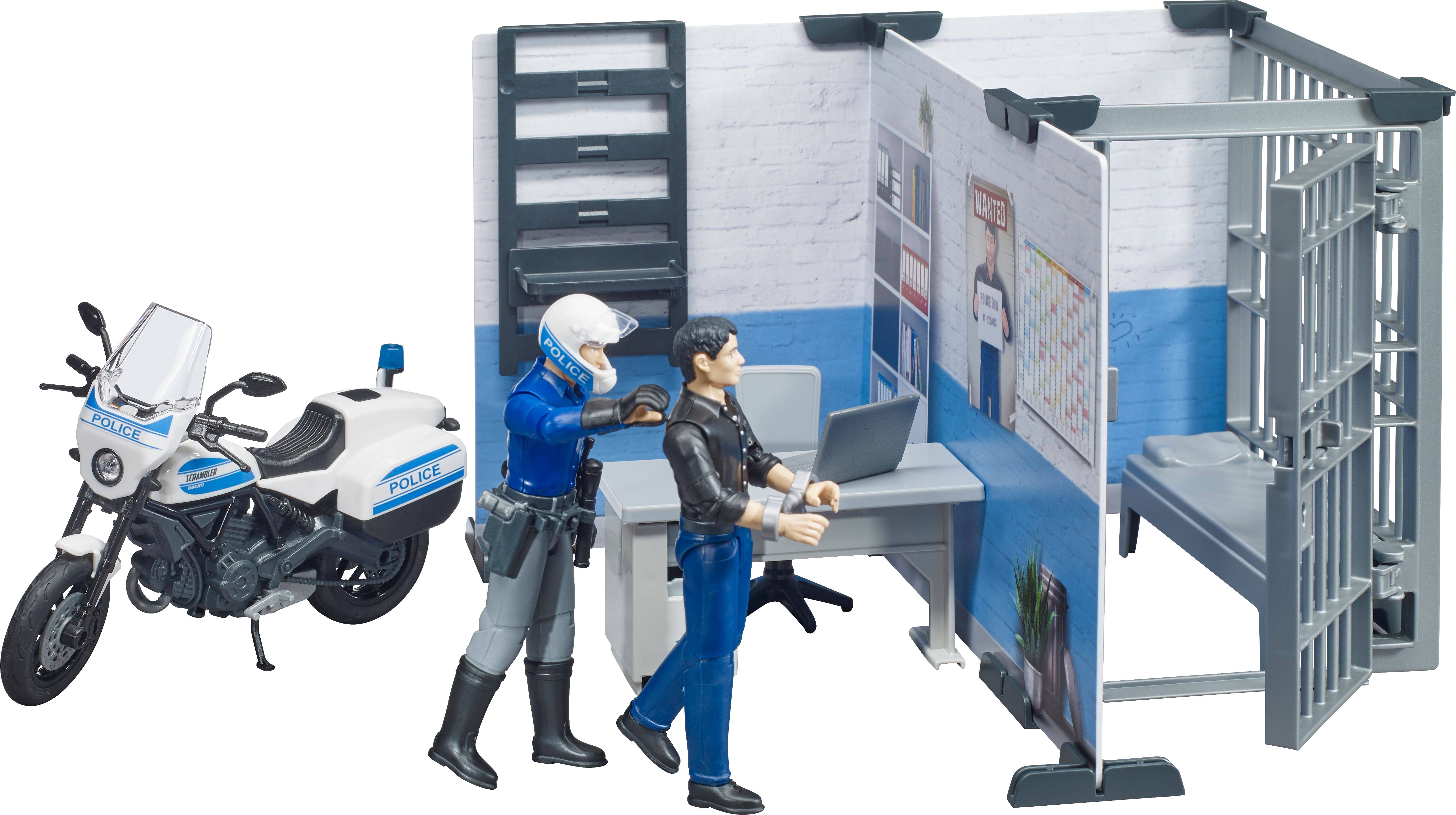 Ein Polizist führt eine Person in eine Zelle in einem Diorama mit einem Bürotisch und einem Laptop. Links steht ein Polizeimotorrad.
