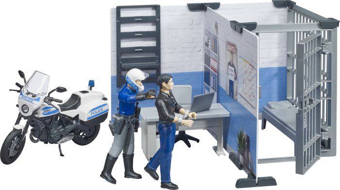 Ein Polizist führt eine Person in ein Büro mit einem Schreibtisch, einem Laptop und einem Gefängnisgitter. Ein Polizeimotorrad steht daneben.