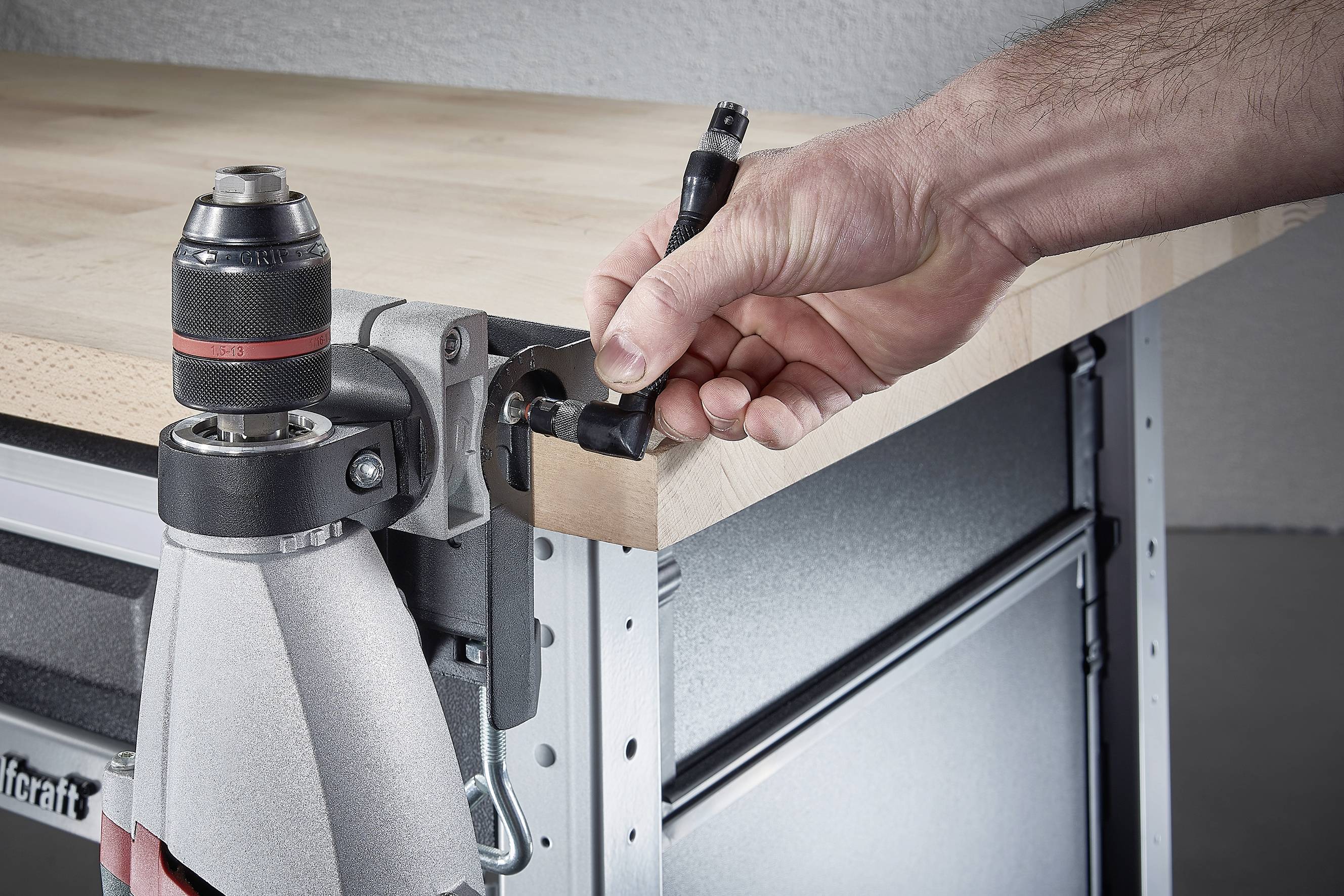 Eine Hand befestigt mithilfe eines Werkzeugs ein Holzelement an einen Metallrahmen auf einer Werkbank.