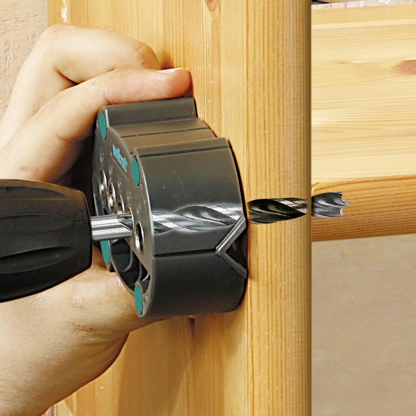 Eine Hand hält eine Bohrmaschine mit einem Lochsägenaufsatz, bohrt ein Loch in ein Holzbrett.