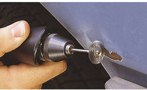 Eine Hand hält einen Bohrer, der eine runde Schleifscheibe verwendet, um Rost von einer Metalloberfläche zu entfernen.