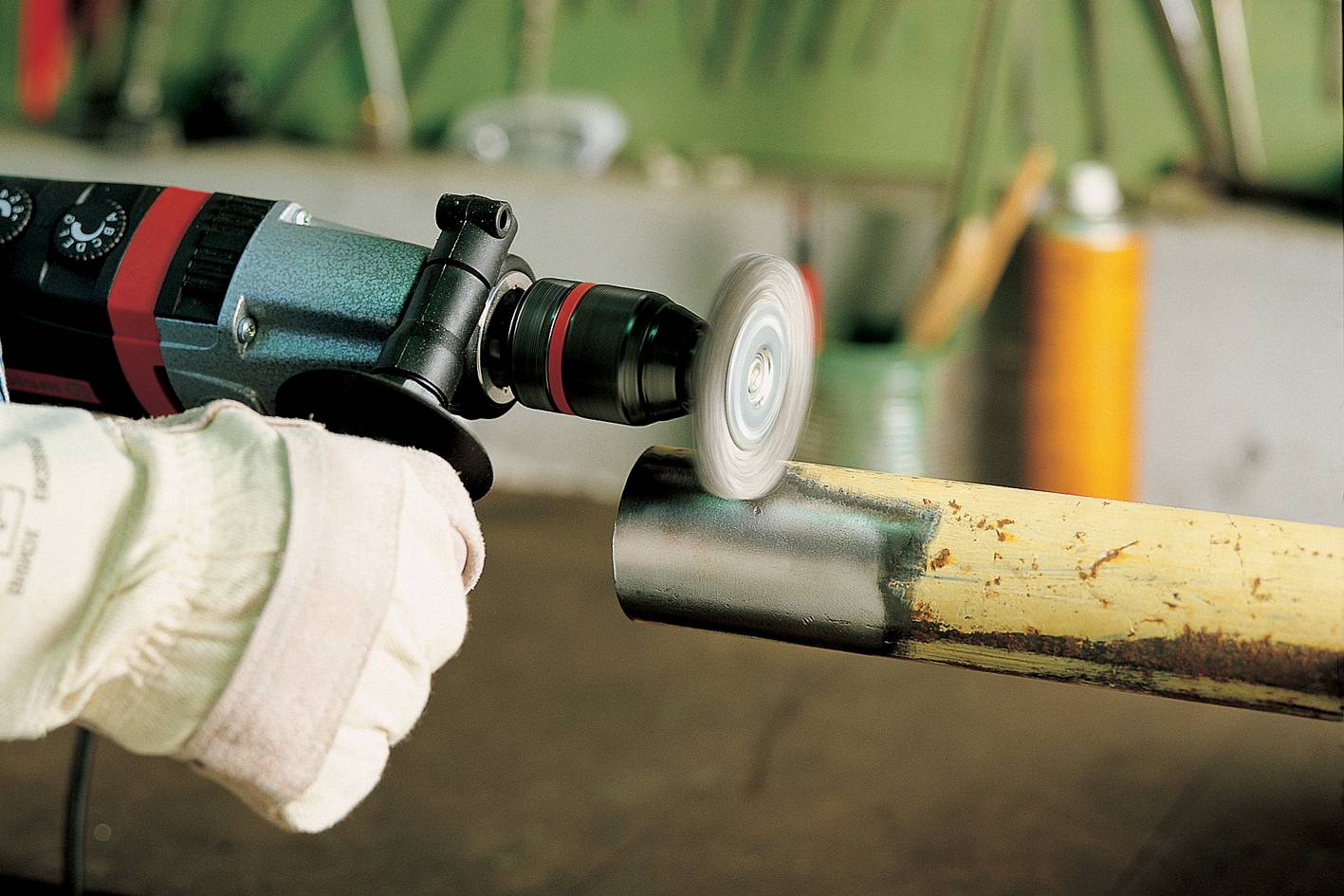 Person schleift Metallrohr mit Winkelschleifer in Werkstatt. Schutzkleidung getragen.