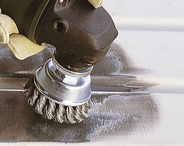 Eine Drahtbürste wird von einer Hand geführt, reinigt eine Metalloberfläche. Der Bereich wird glatt und glänzend.