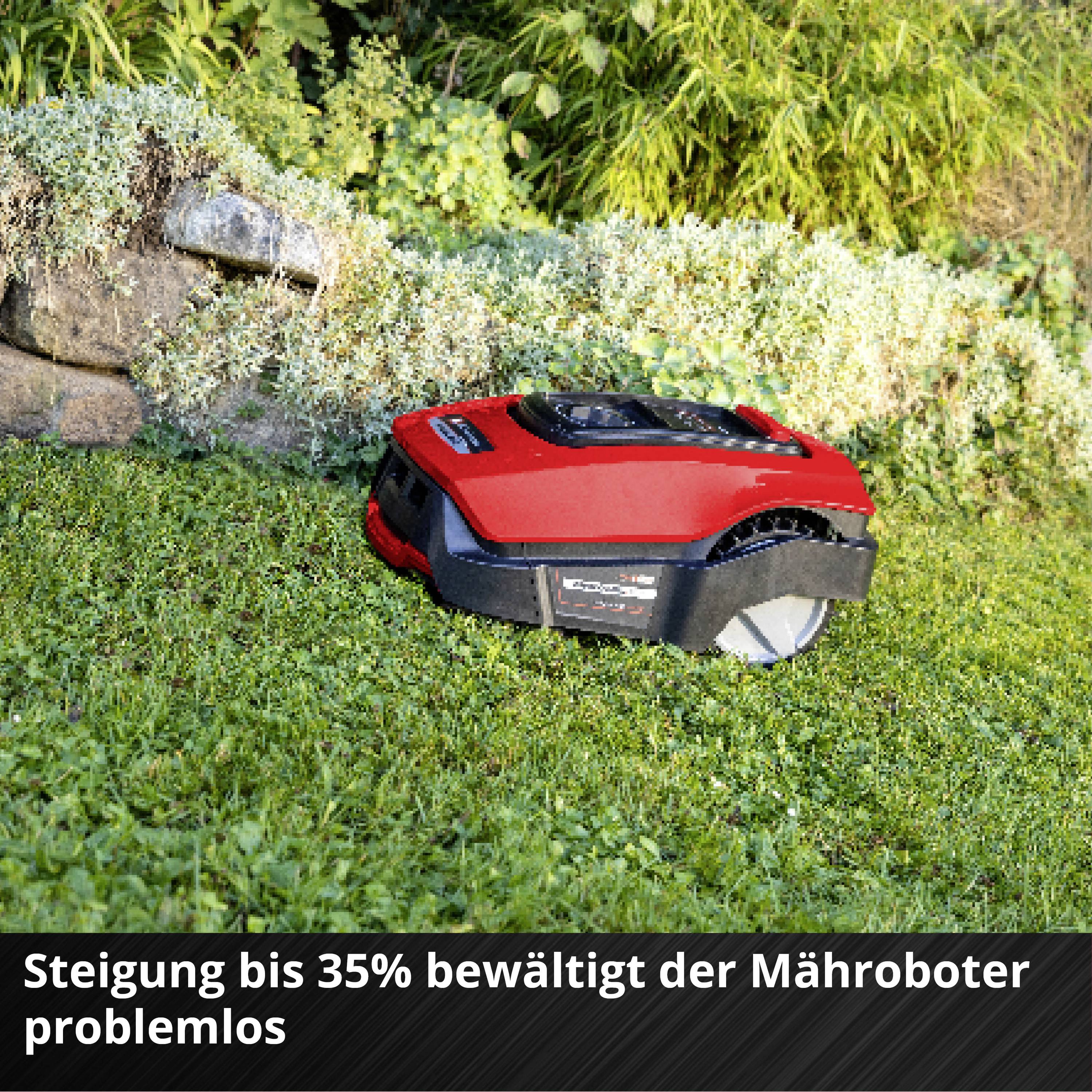 Ein roter Mähroboter mäht selbstständig Gras auf einem grünen Rasen neben einer Steinwand. Text: 'Steigung bis 35% bewältigt der Mähroboter problemlos'.