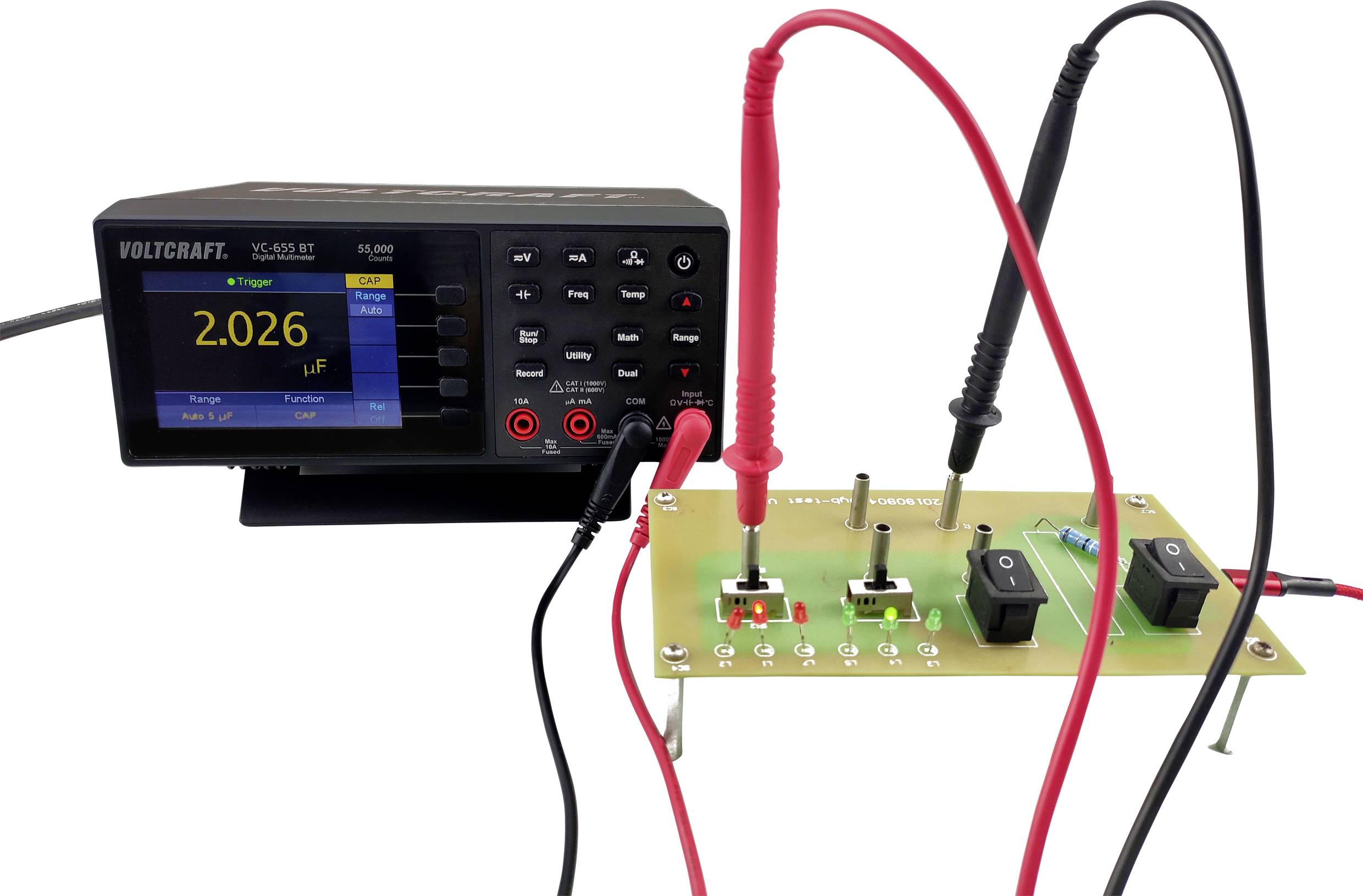 Ein digitales Messgerät misst elektronische Komponenten auf einer Leiterplatte. Ein Bildschirm zeigt '2.026 µF'.