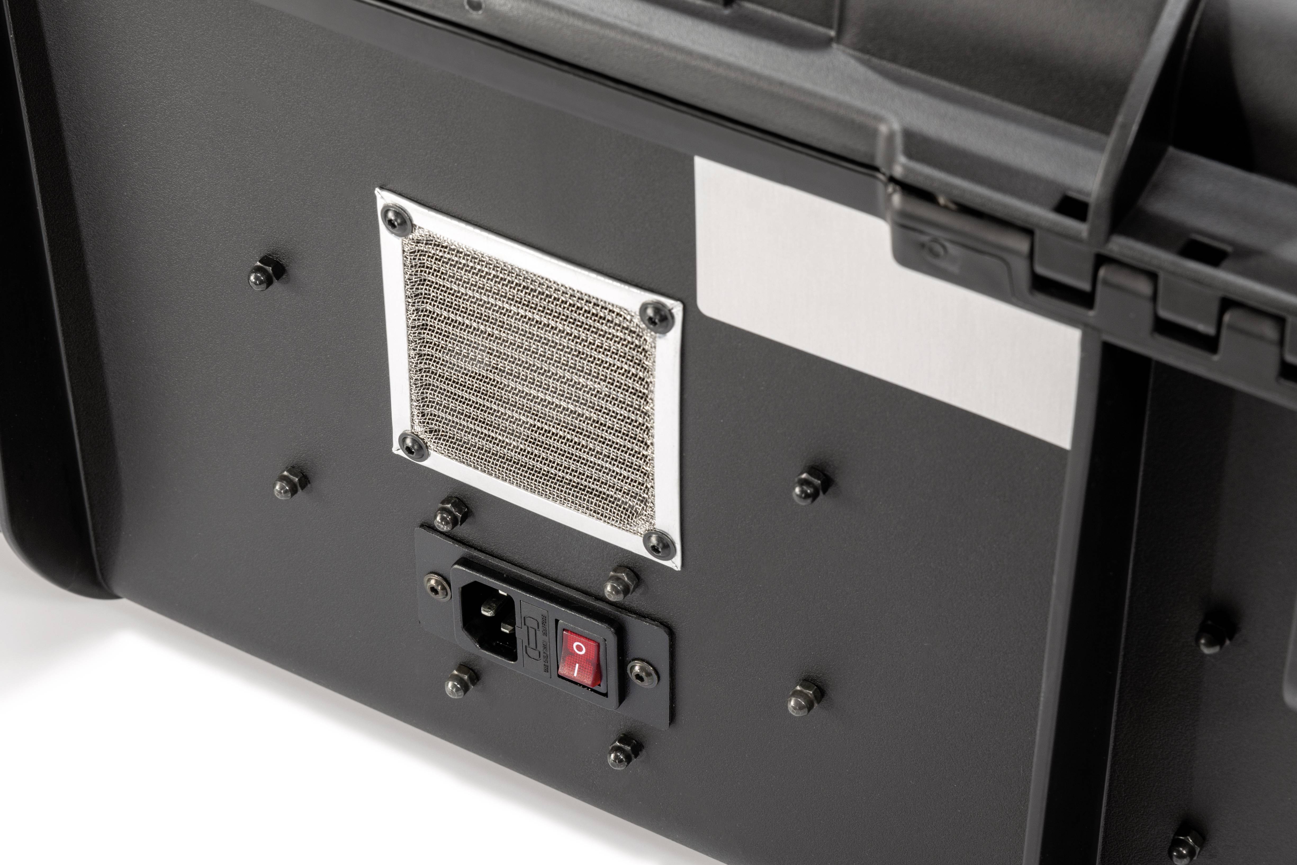 Detailaufnahme der Rückseite eines technischen Geräts, mit einem Luftgitter und einem roten Ein-/Ausschalter unter einer Steckdose.