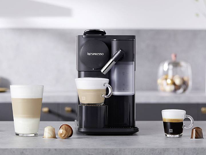 Eine schwarze Kaffeemaschine bereitet Kaffee zu. Auf einer grauen Küchenarbeitsplatte stehen drei Tassen mit verschiedenen Kaffeesorten.