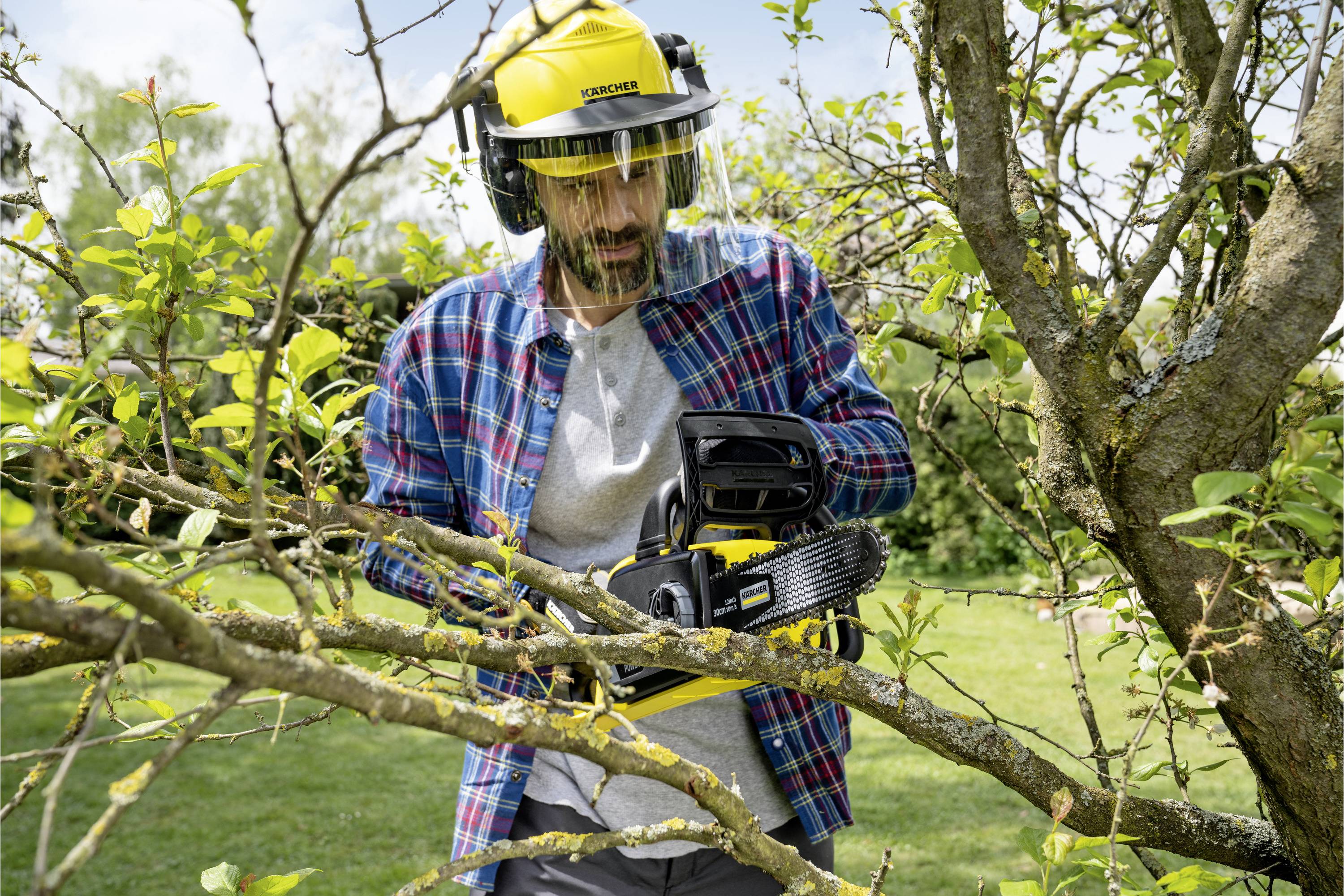 Ein Mann in Schutzkleidung schneidet mit einer Kettensäge Äste von einem Baum in einem Garten.
