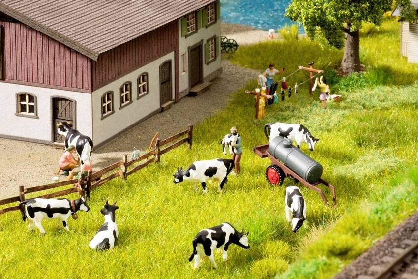 Kühe weiden auf einer Wiese neben einem Bauernhof; Menschen arbeiten im Hintergrund. Ländliche Szenen mit Grünflächen und Bauernhofgebäuden.