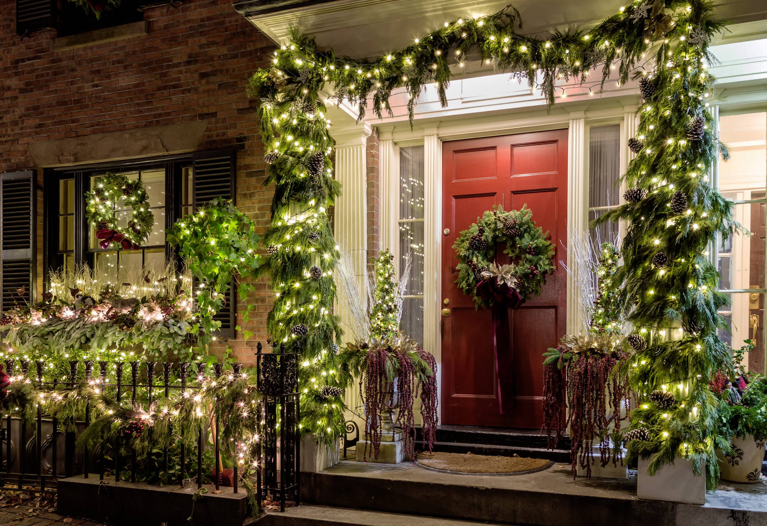 Ein festlich geschmückter Hauseingang mit roten Türen, umrahmt von leuchtenden Weihnachtslichtern und Kränzen. Einladende Atmosphäre.