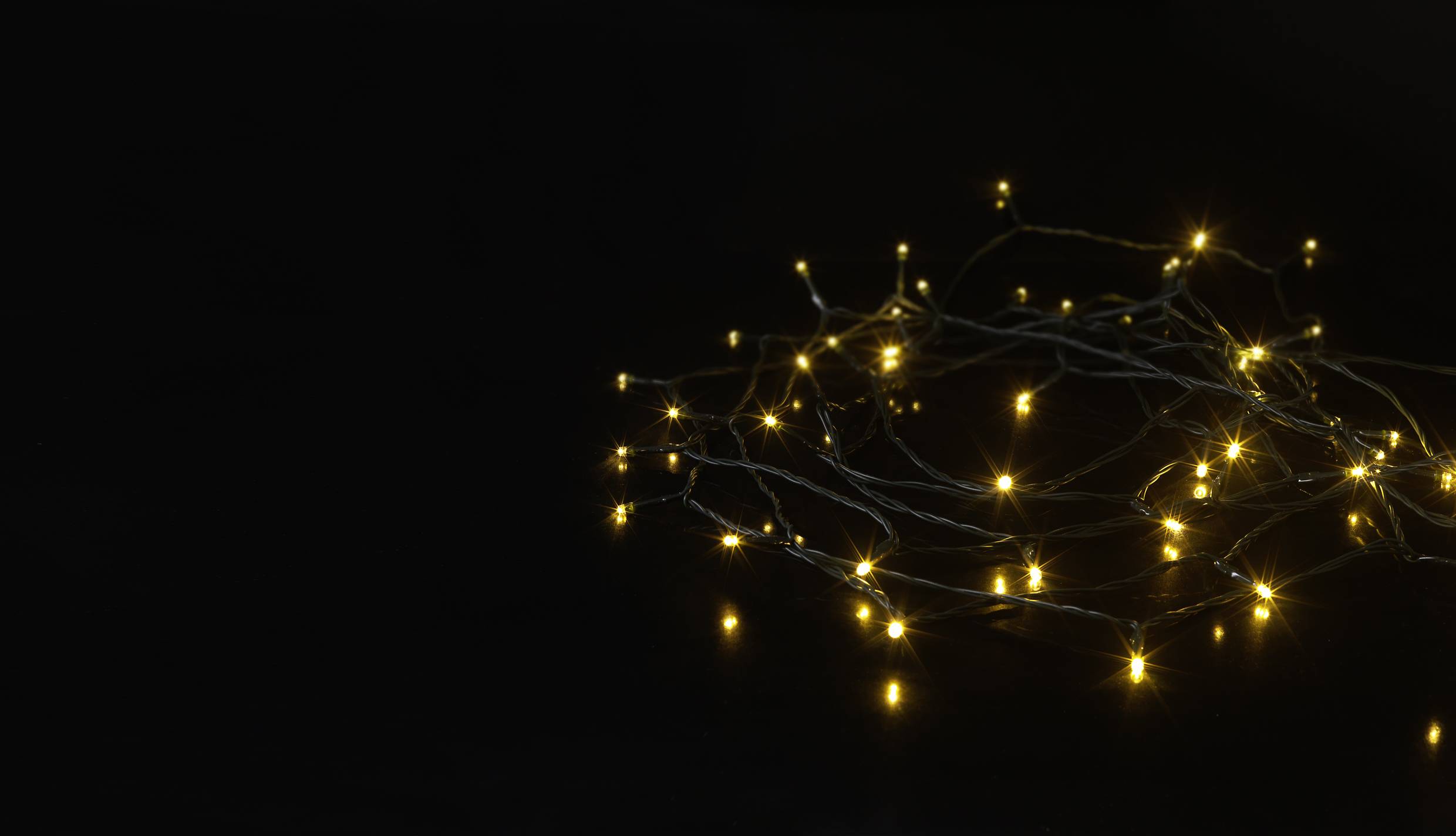 Lichterkette mit kleinen leuchtenden gelben Lichtern, die gleichmäßig auf dunklem Hintergrund verteilt sind.