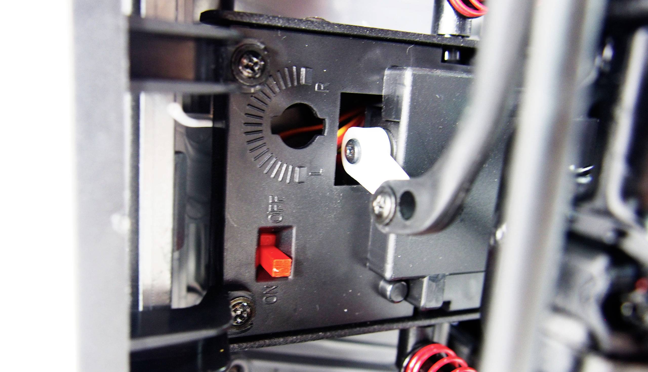 Nahaufnahme eines mechanischen Schalters mit rotem Hebel in der 'Aus'-Position, umgeben von Metallstreben und Kabeln.
