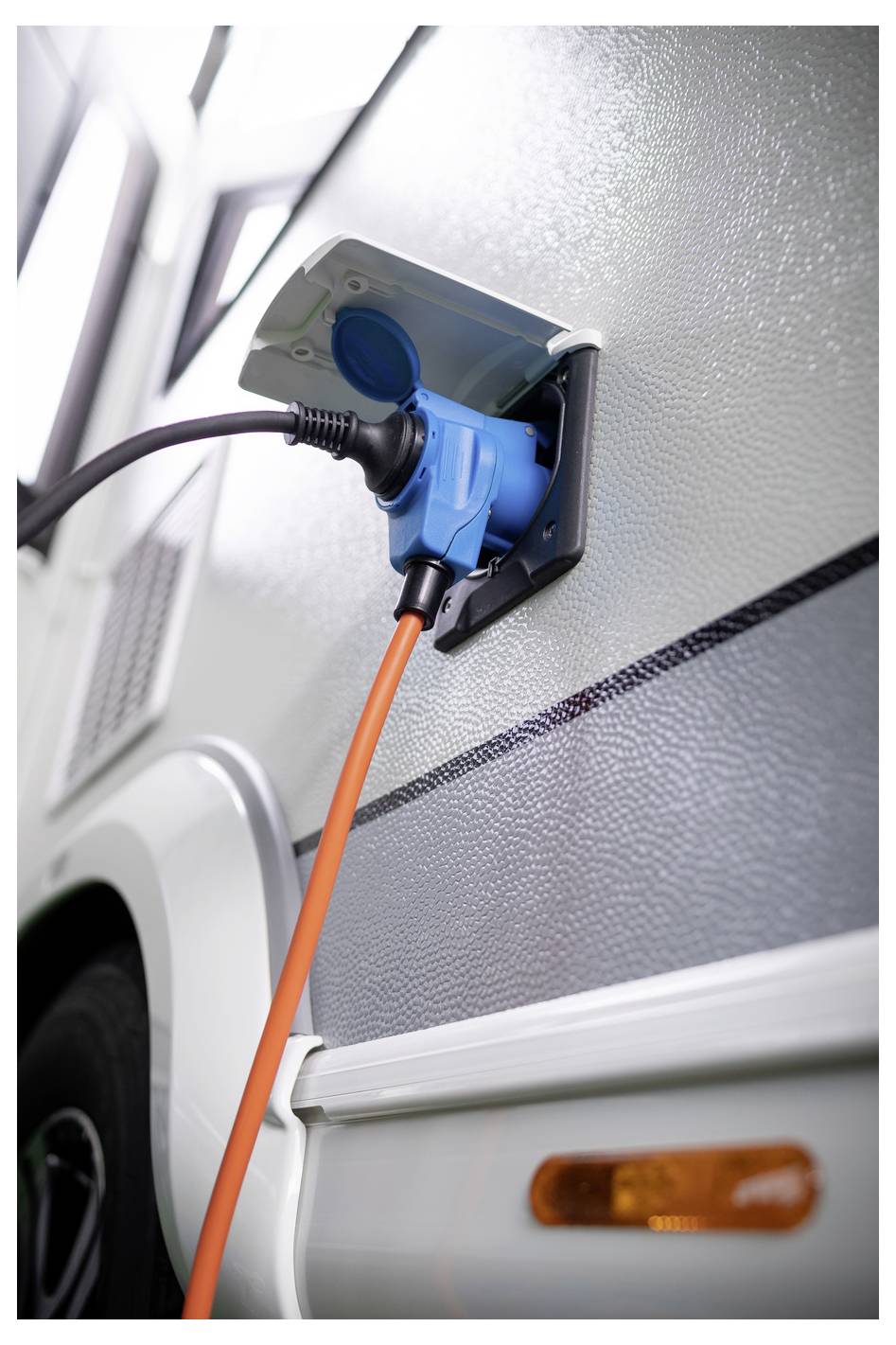 Elektrofahrzeug-Ladekabel in die Seite eines silbernen Wohnmobils oder Wohnwagens gesteckt, mit einem orangefarbenen Kabel, das mit der Steckdose verbunden ist.