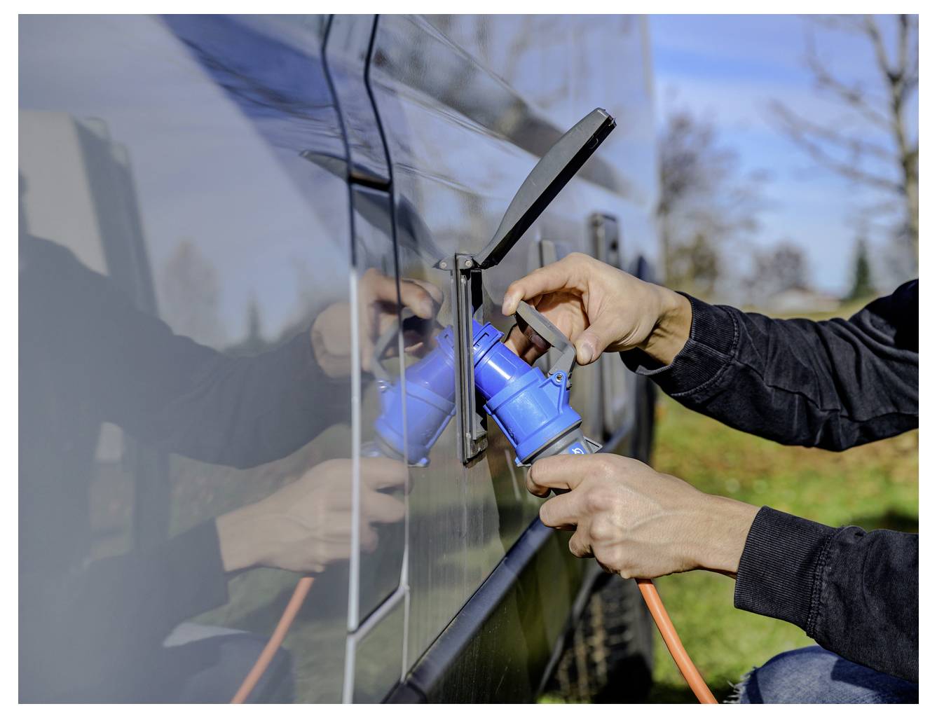 Person, die ein blaues Stromkabel in den Ladeanschluss eines Elektrofahrzeugs im Freien einsteckt.
