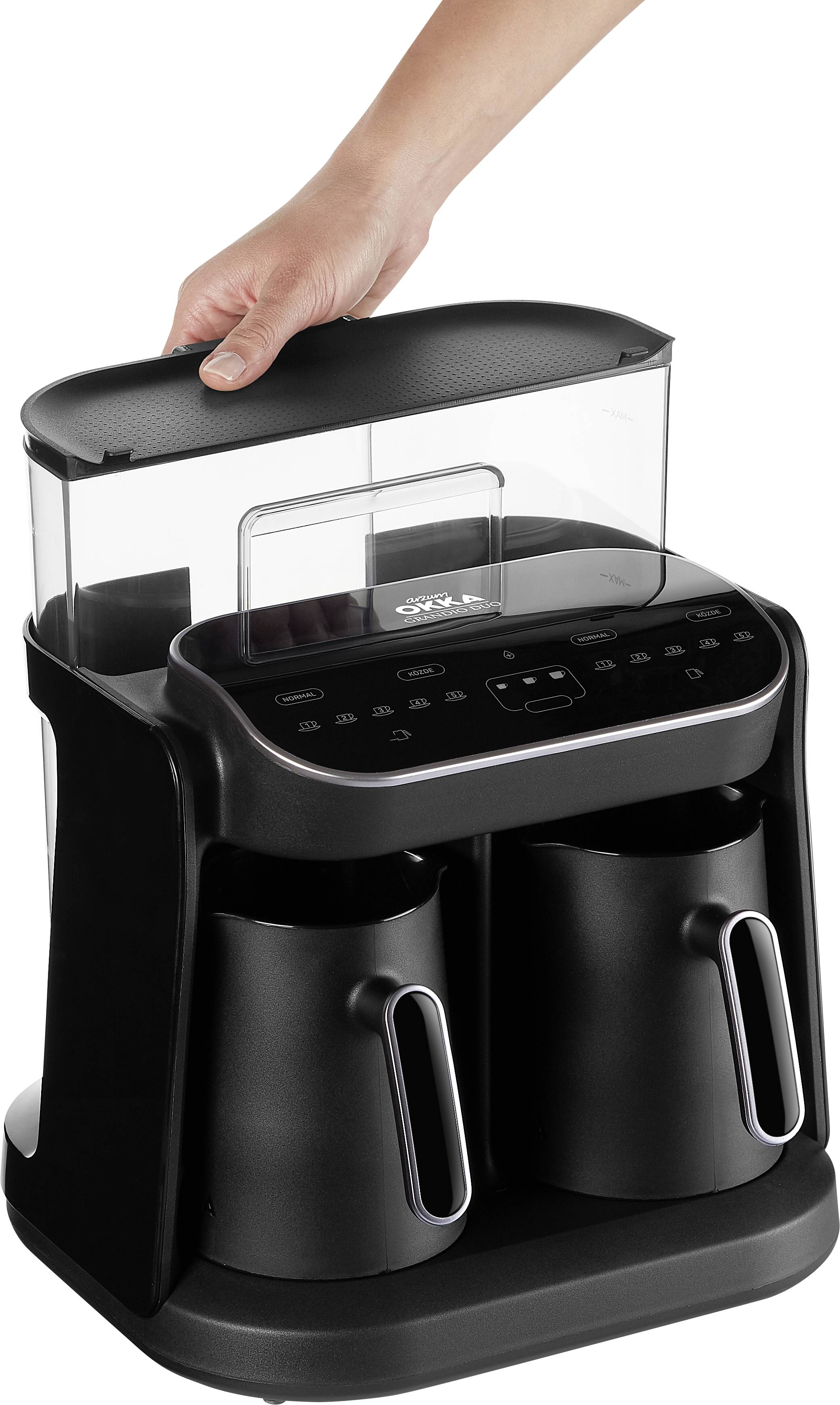 Eine Hand hebt einen Deckel von einer schwarzen Kaffeemaschine mit zwei Kannen.