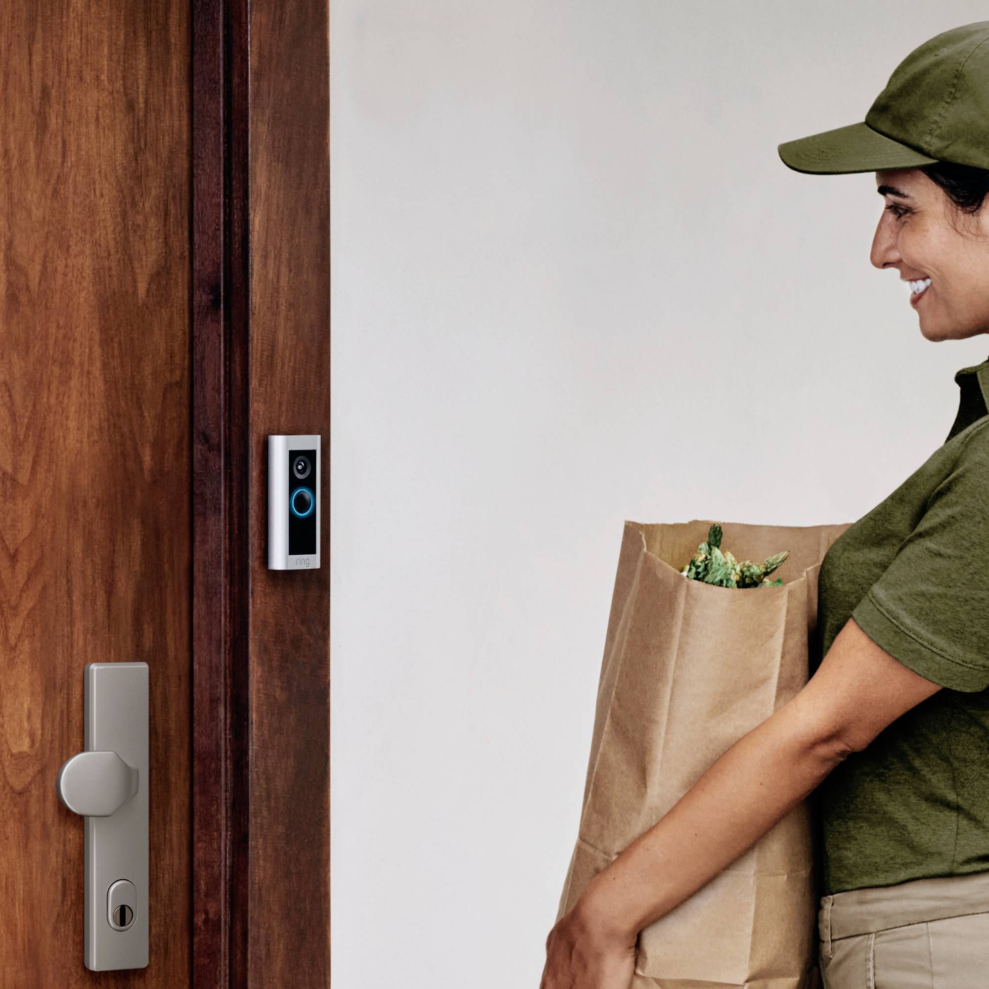 Eine Person in Uniform hält eine Papiertüte vor einer Tür mit einer Türklingelkamera und scheint einen Lieferservice durchzuführen.