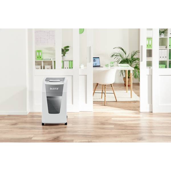 Büro mit hellen Holzböden und weißen Regalen, im Vordergrund ein Papiervernichter, im Hintergrund ein Schreibtisch mit einem Laptop.