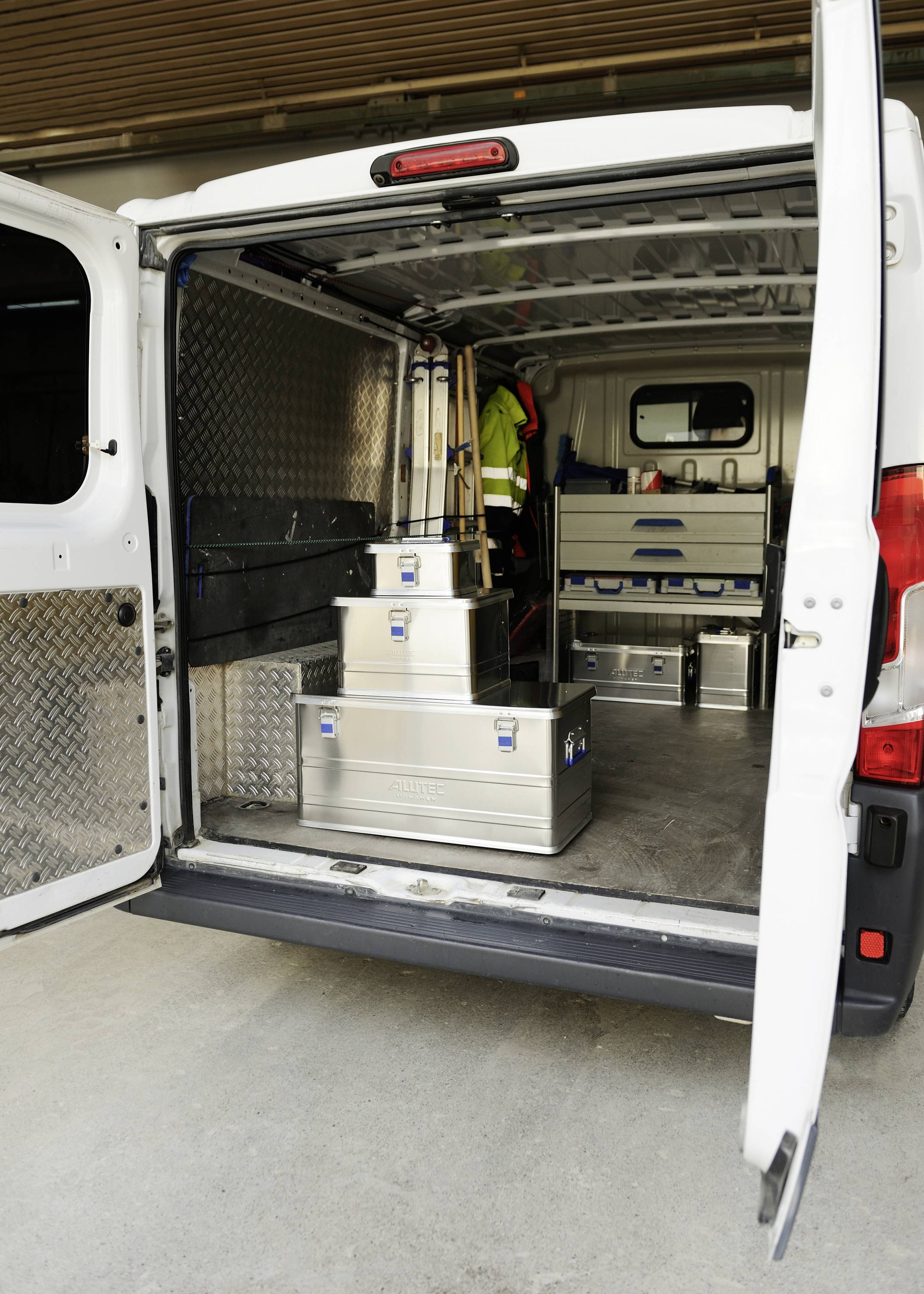 Ein weißer Transporter mit offener Hintertür zeigt mehrere Metallkisten und Ausrüstungen im Laderaum, bereit für den Einsatz.