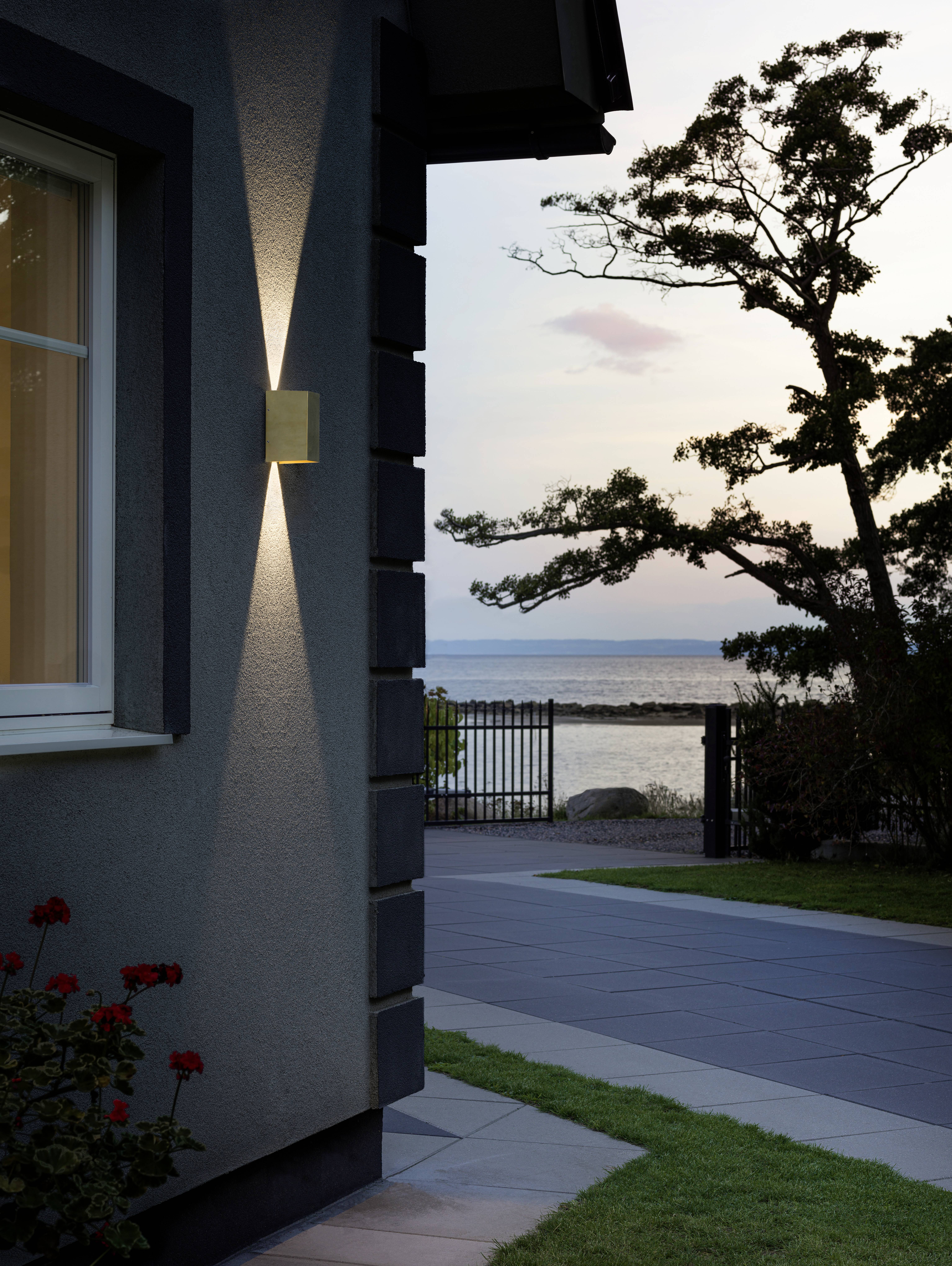 Ein beleuchtetes Haus bei Sonnenuntergang mit Blick auf einen ruhigen See im Hintergrund, nahe einem Baum und einem Garten.