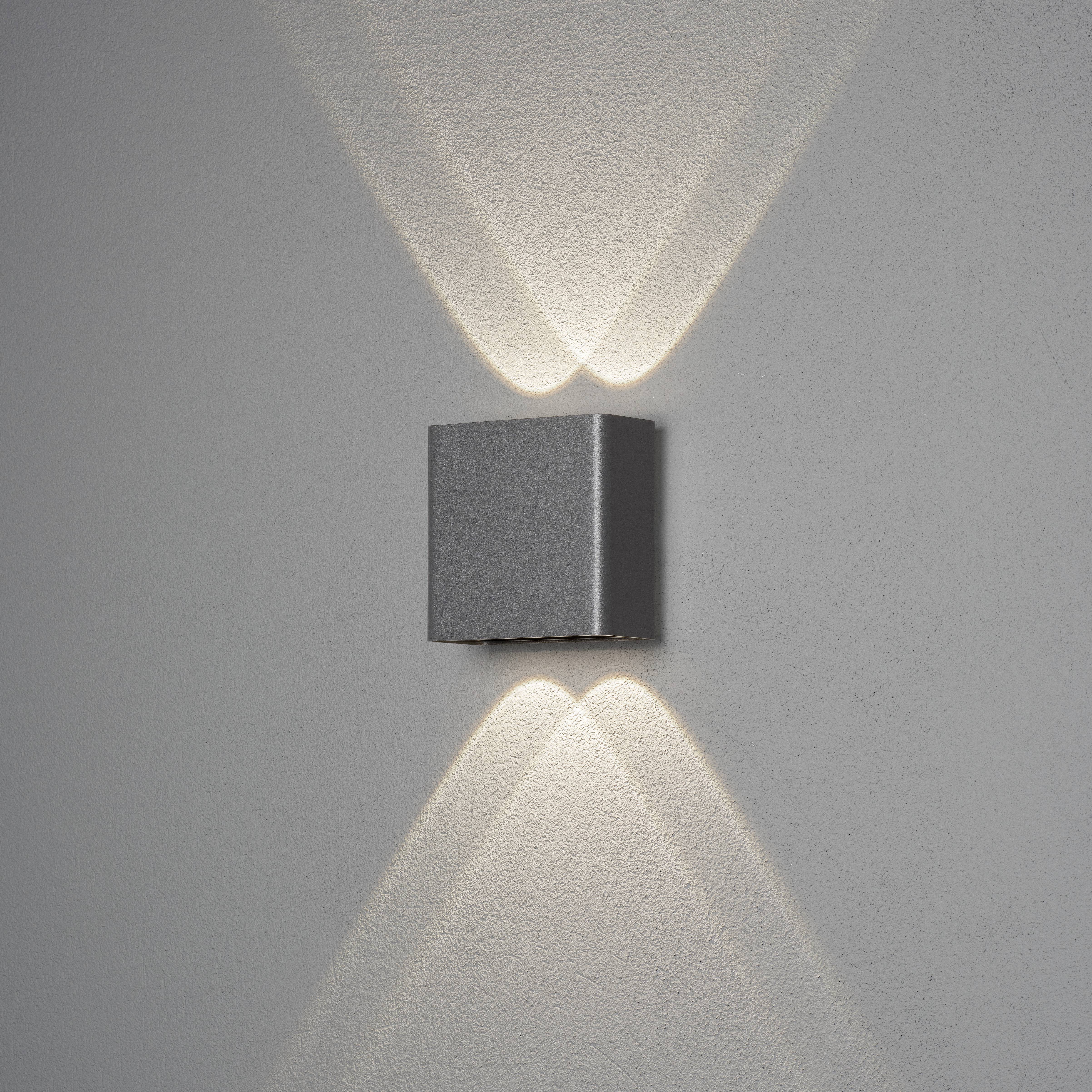 Wandlampe mit quadratischem Gehäuse strahlt weiches Licht nach oben und unten, erzeugt symmetrische Lichtmuster an der Wand.