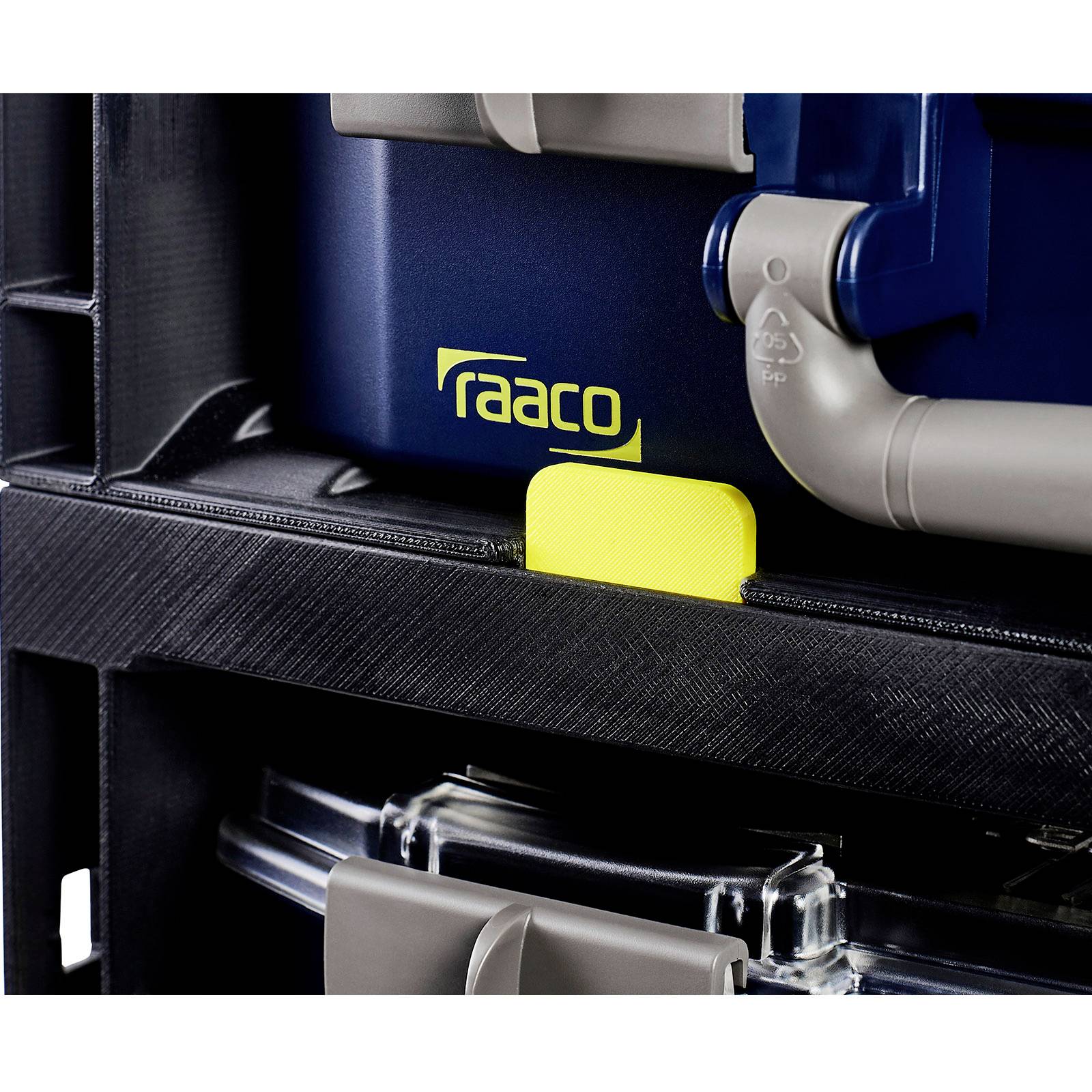 Eine Nahaufnahme eines 'raaco' Lagerungssystems, die einen Verschließmechanismus und einen Teil eines Griffs zeigt, wobei das Markenbrandlogo in Gelb hervorgehoben wird.