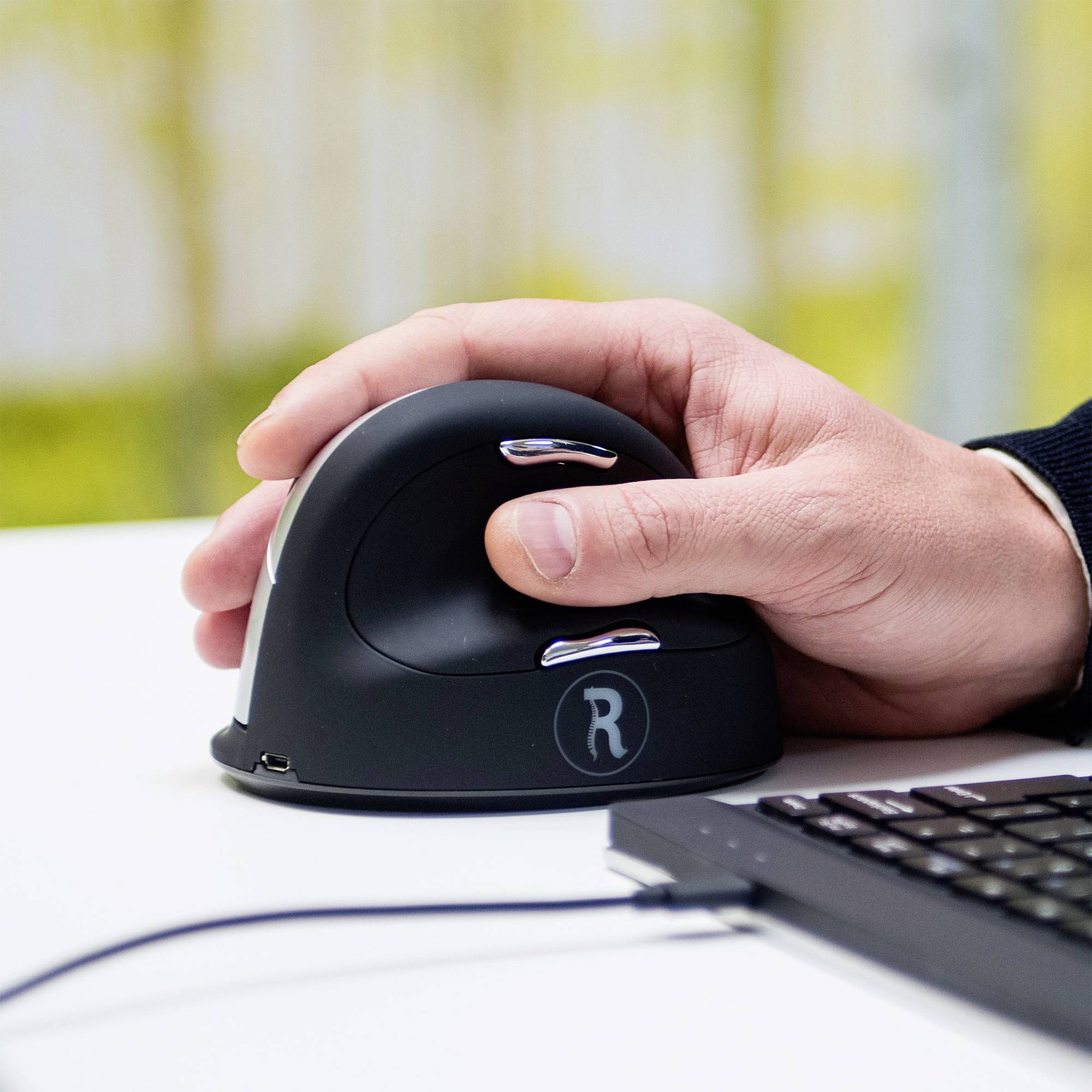 Eine Person bedient eine ergonomische vertikale Maus neben einer Tastatur. Die Handhaltung wirkt entspannt und verhindert übermäßige Belastung.