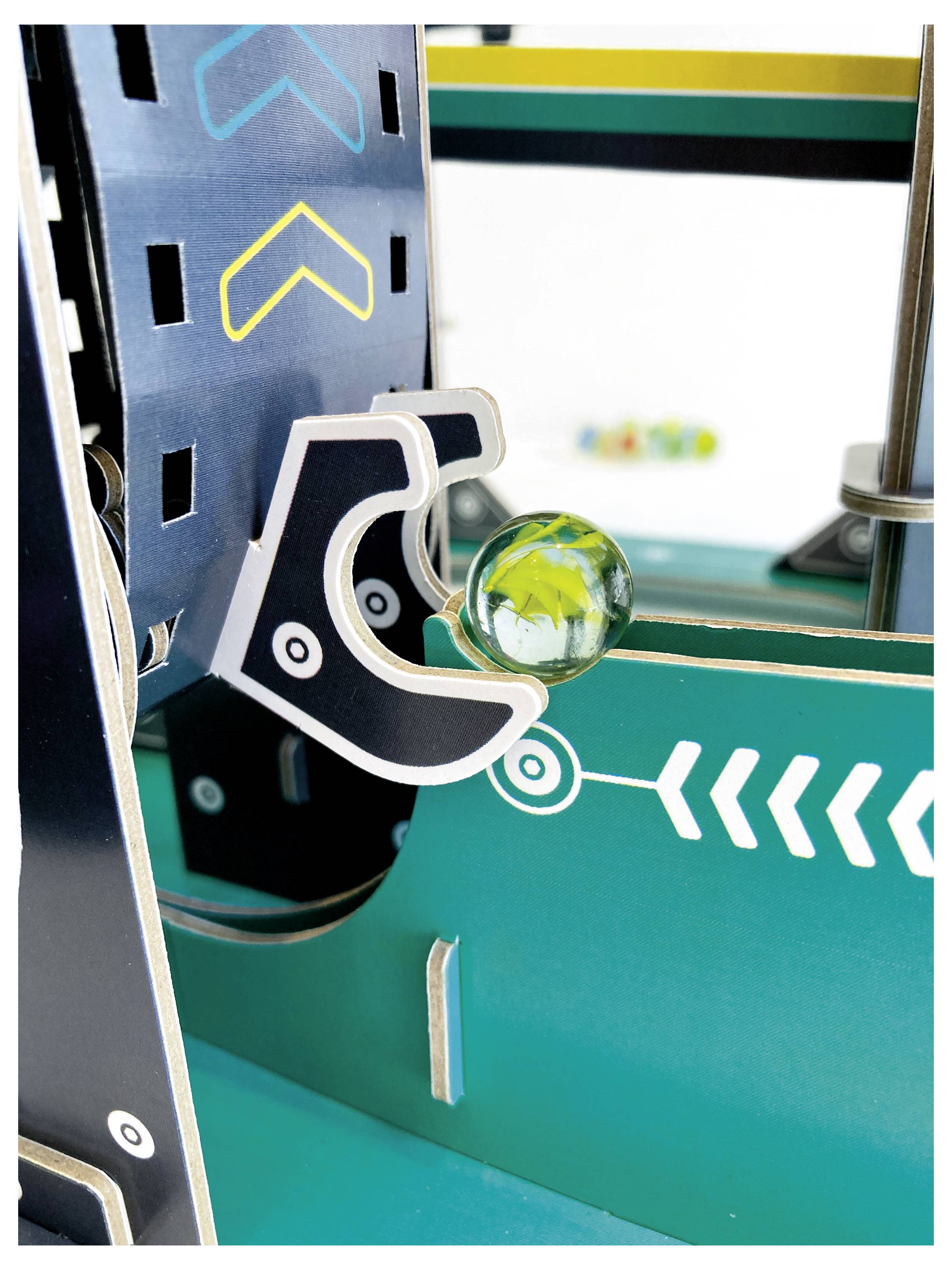Nahaufnahme einer mechanischen, im Arcade-Stil gehaltenen Kralle, die eine klare Glaskugel in einer türkisfarbenen Spielmaschine hält.