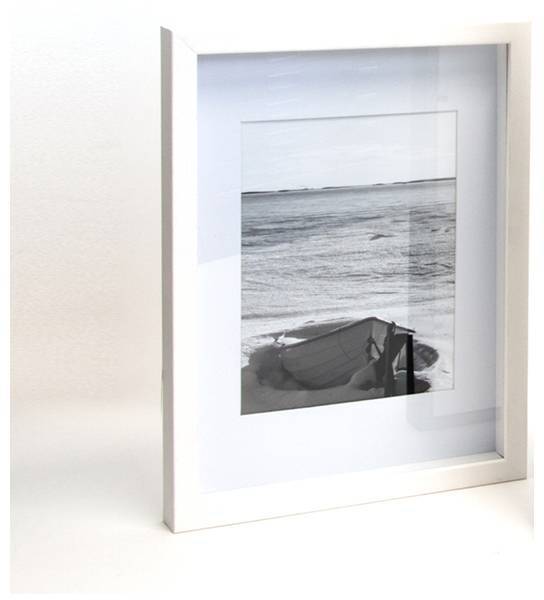 Ein gerahmtes Schwarz-Weiß-Foto zeigt ein kleines Boot am Strand mit weitem Meer und Himmel im Hintergrund.