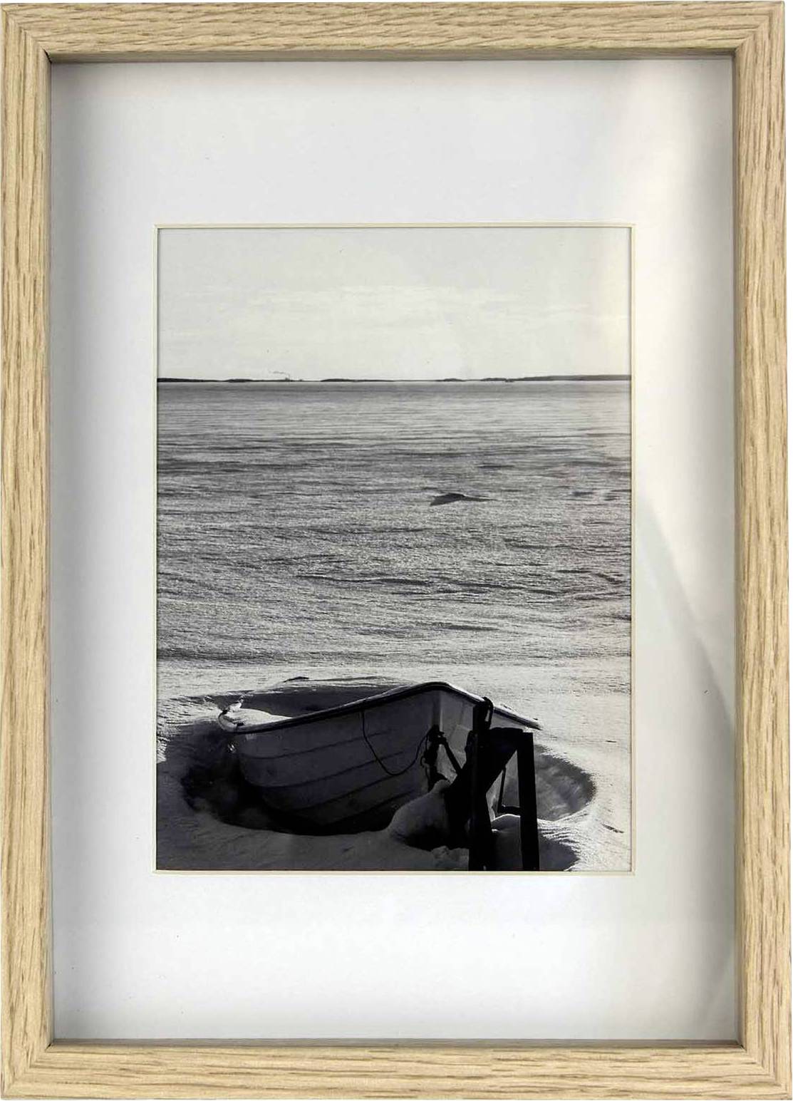 Ein Holzboot liegt im gefrorenen, schneebedeckten Ufer. Im Hintergrund erstreckt sich eine weite, eisige Landschaft unter bewölktem Himmel.