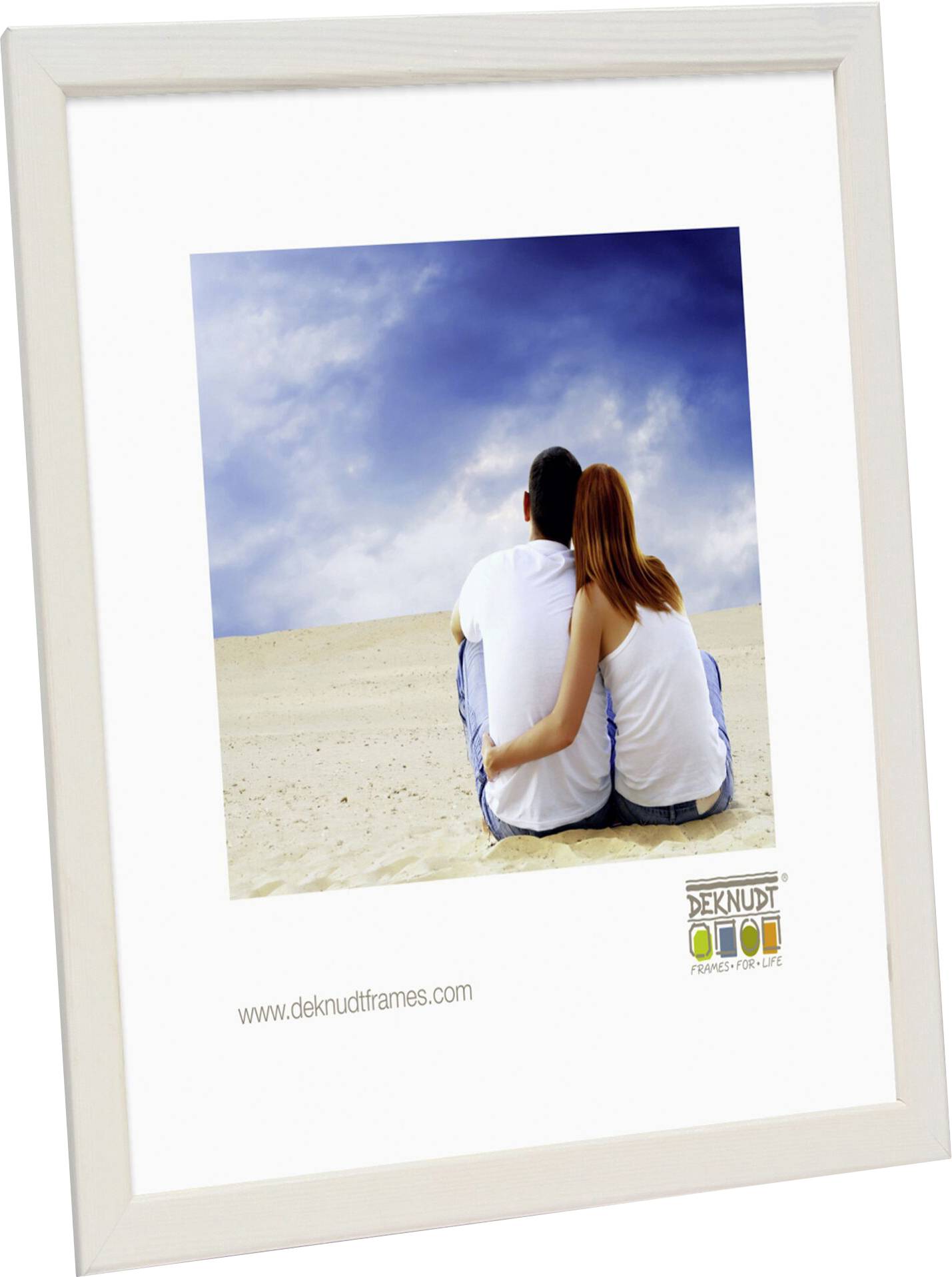 Ein Paar sitzt eng umschlungen auf einem sandigen Strand, blickt in die Ferne unter einem bewölkten Himmel.