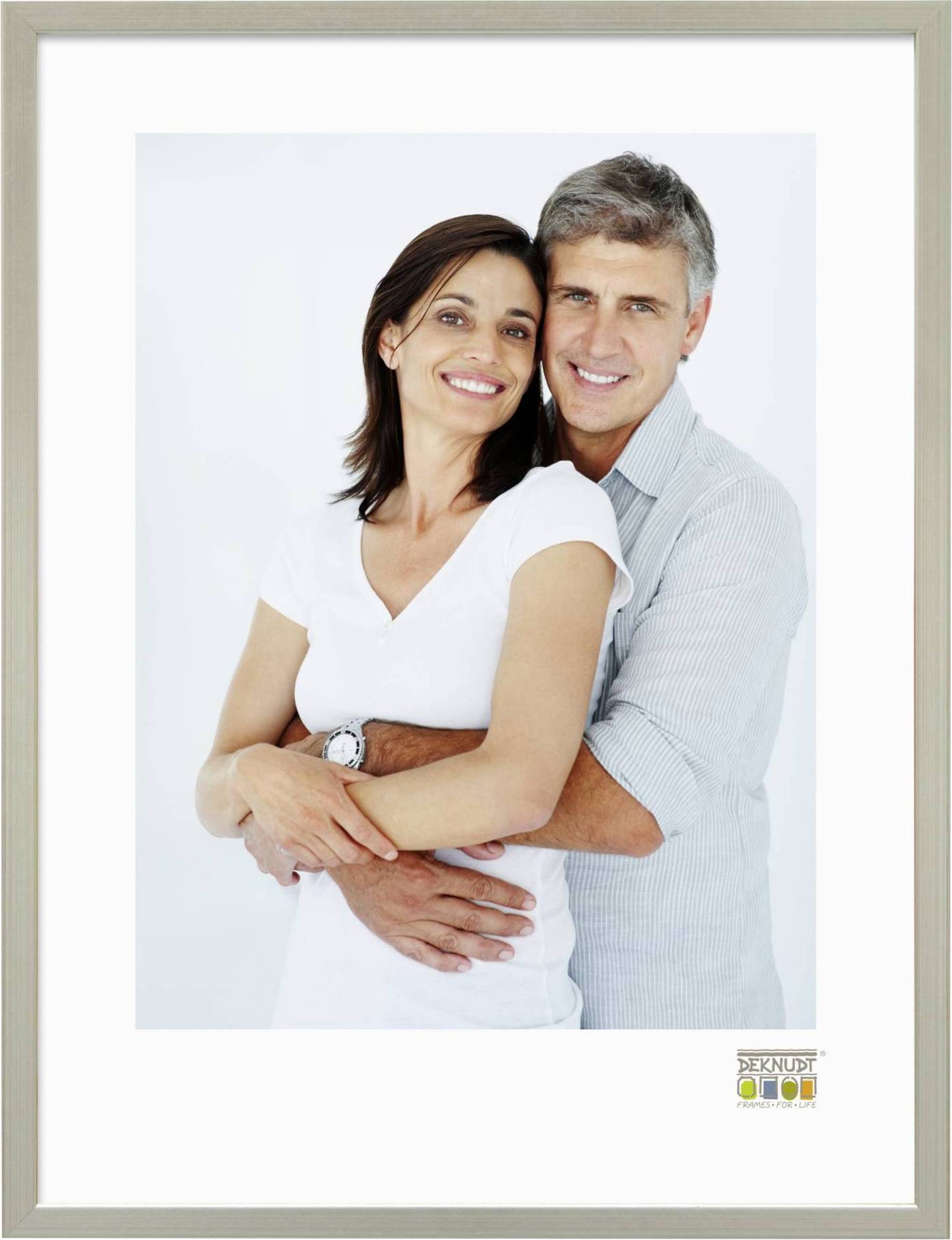 Ein lächelndes Paar umarmt sich vor einem neutralen Hintergrund, beide in Freizeitkleidung. Sie wirken entspannt und glücklich.