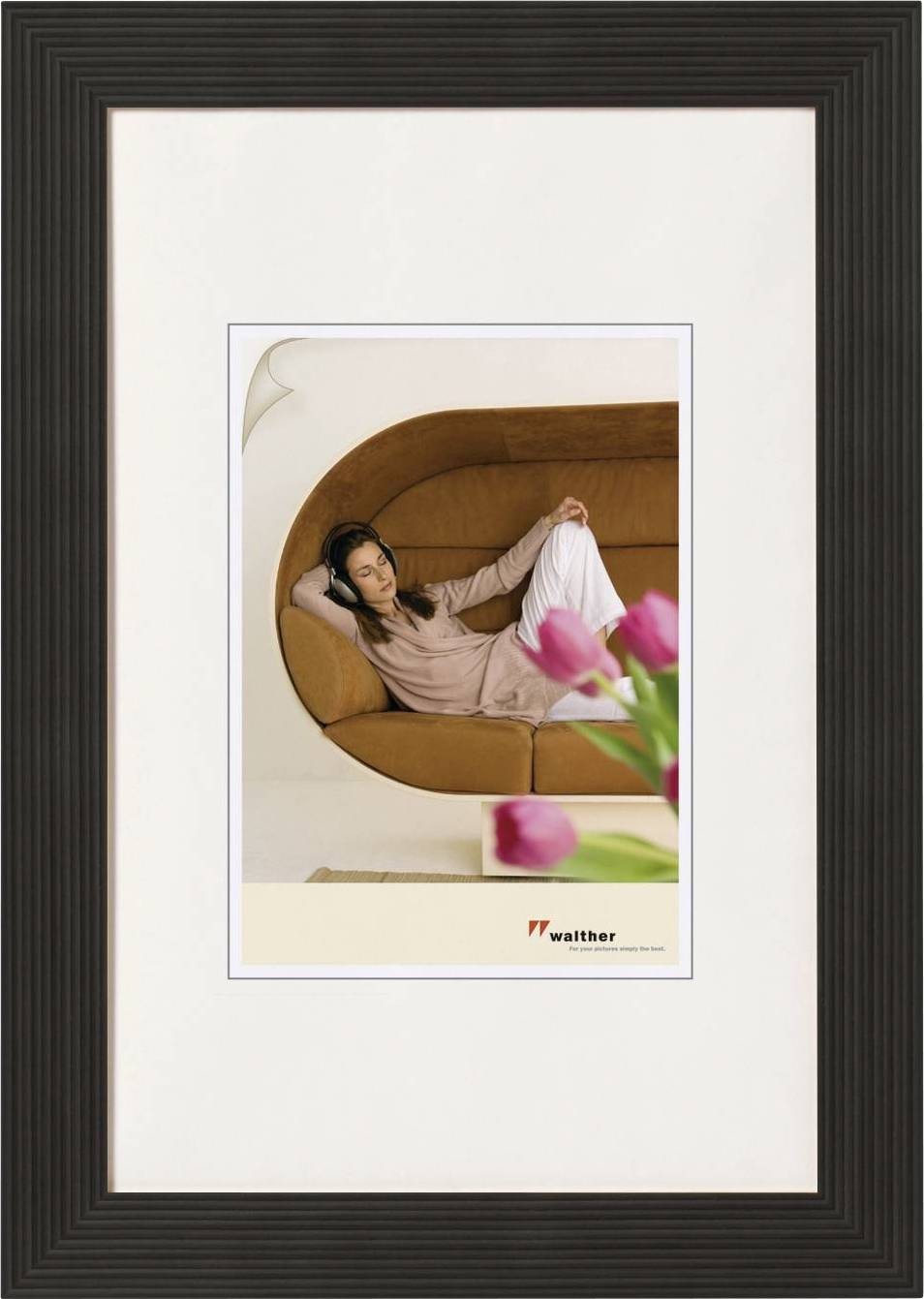 Eine Person entspannt auf einem braunen Sofa, während im Vordergrund rosa Tulpen zu sehen sind.