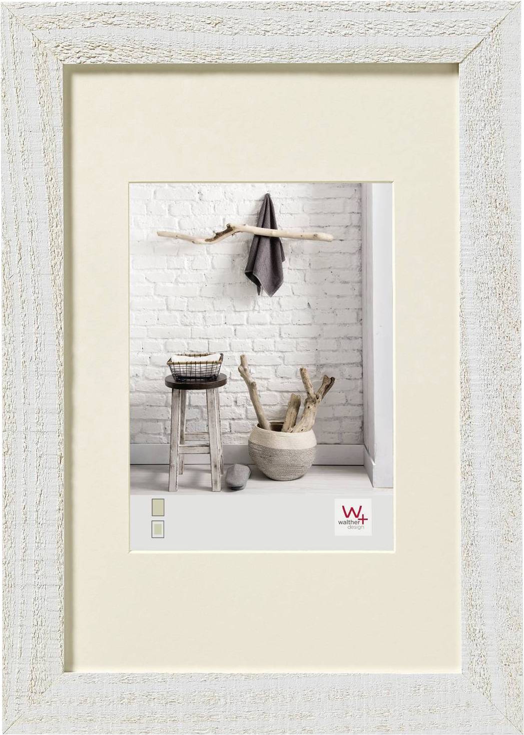 Holzrahmen mit einem Bild eines rustikalen Interieurs: Hocker, Korb, und Schale aus Holz vor einer weißen Backsteinwand.