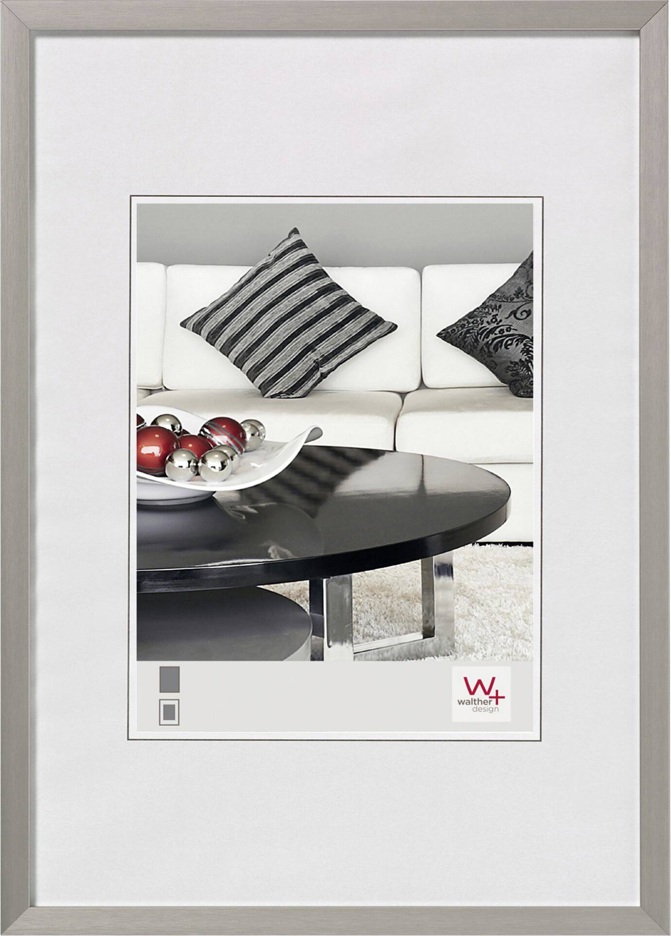 Ein eleganter Wohnraum mit weißem Sofa, schwarz-weißen Kissen und einem runden Couchtisch mit silberroten Dekokugeln.