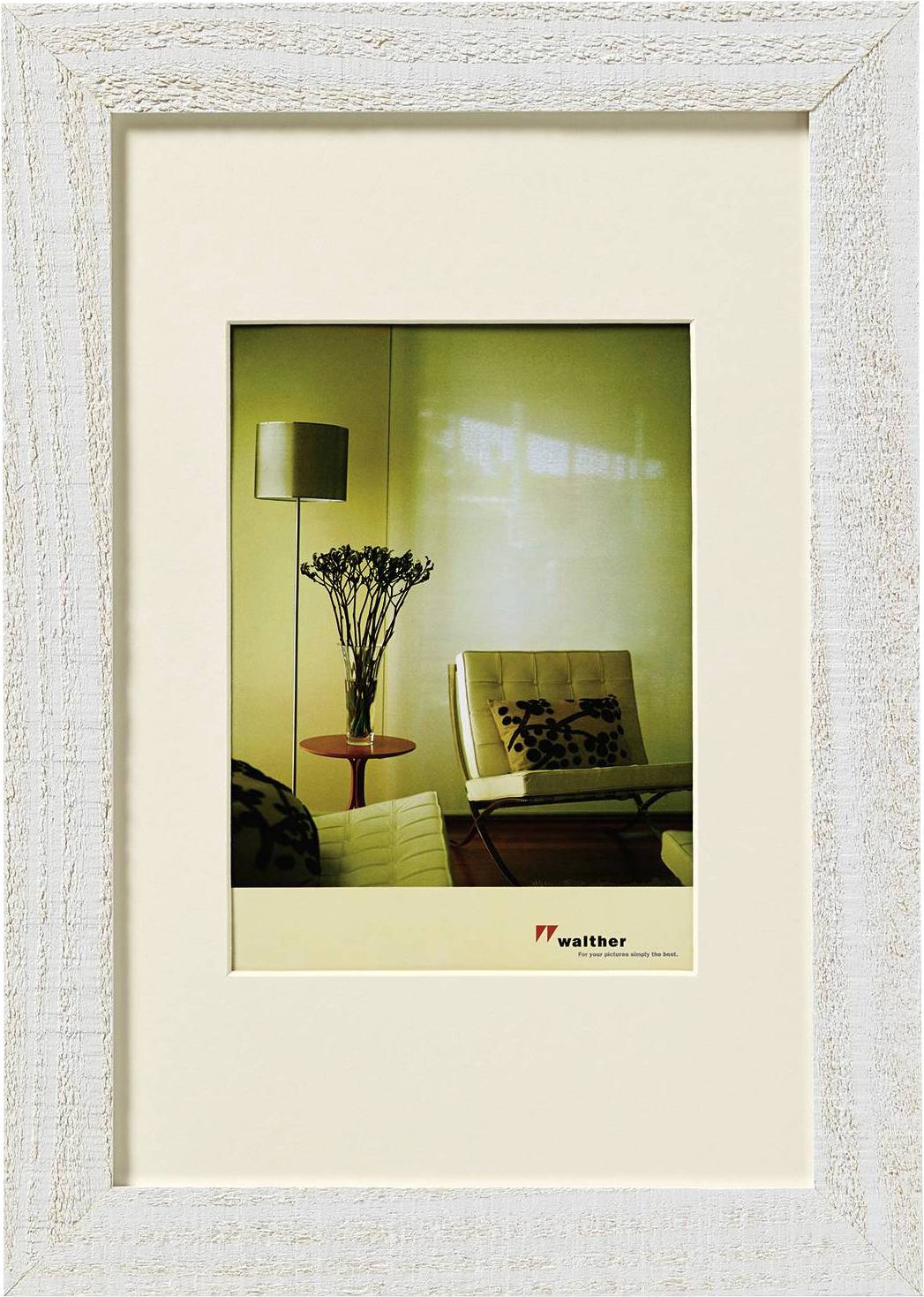 Ein Wohnzimmer mit zwei Sesseln, einem runden Tisch mit einer Vase, und einer Stehlampe. Foto in einem weißen Holzrahmen.