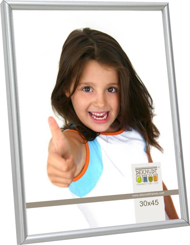 Mädchen mit braunem Haar zeigt Daumen hoch und lächelt in die Kamera. Rahmenetikett zeigt 'Deknudt Frames' und Größe '30x45'.