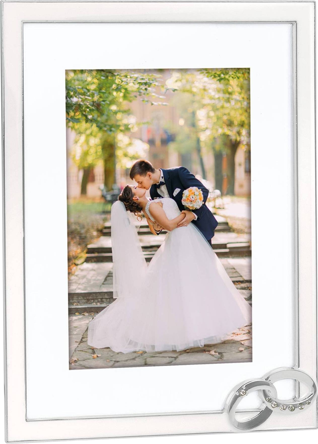 Ein Brautpaar in Hochzeitskleidung tanzt in einem sonnigen Park. Der Bräutigam hält einen Blumenstrauß, während sie sich küssen.