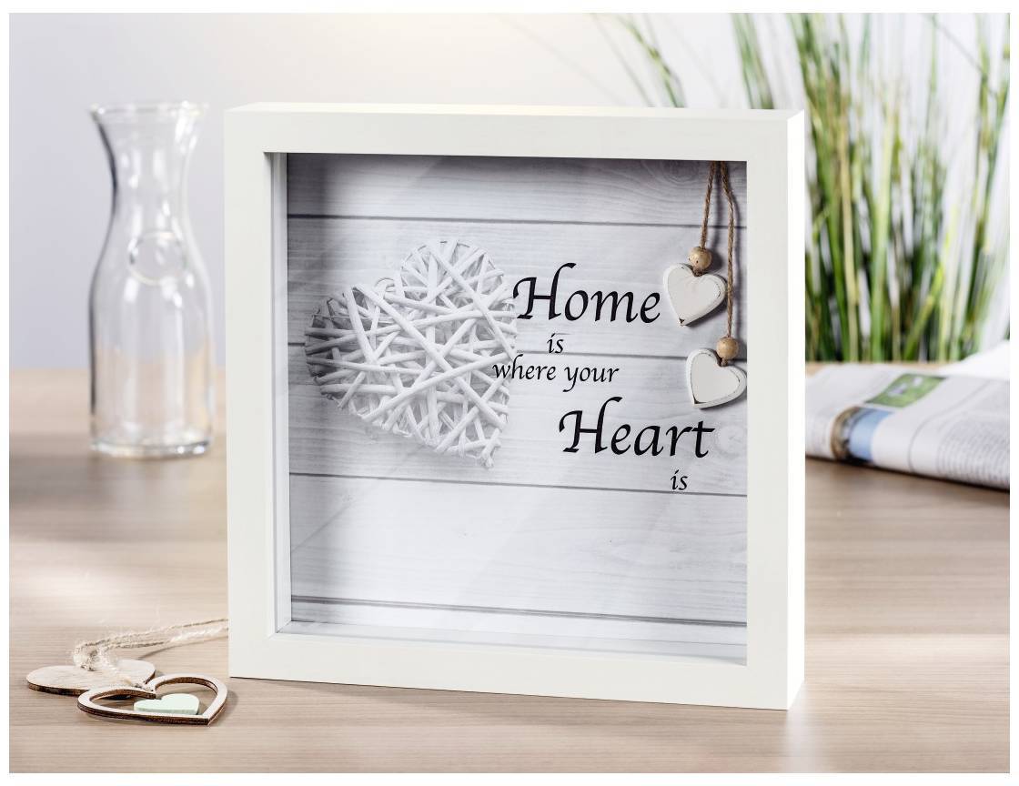 Ein eingerahmtes Bild zeigt den Text 'Home is where your Heart is' mit einem weißen Herz aus Holz als Dekoration im Hintergrund.